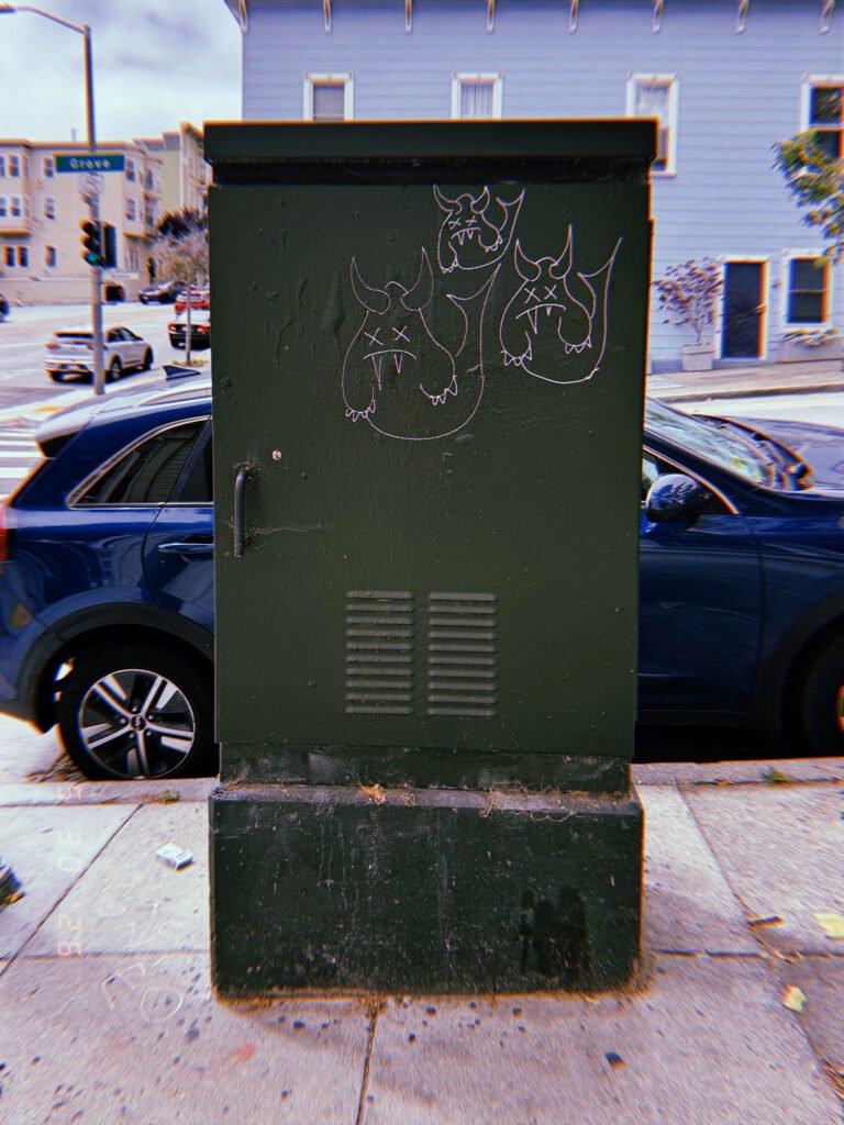 A dark green utility cabinet installed on a San Francisco sidewalk, marked with small graffiti drawings and enclosing electrical or communications infrastructure behind a metal access door.
