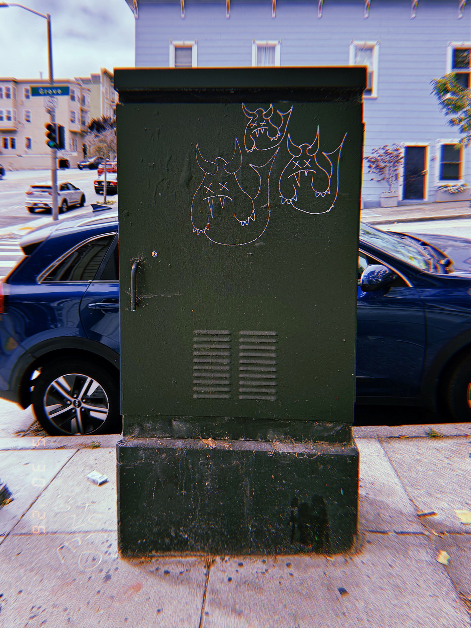 A dark green utility cabinet installed on a San Francisco sidewalk, marked with small graffiti drawings and enclosing electrical or communications infrastructure behind a metal access door.