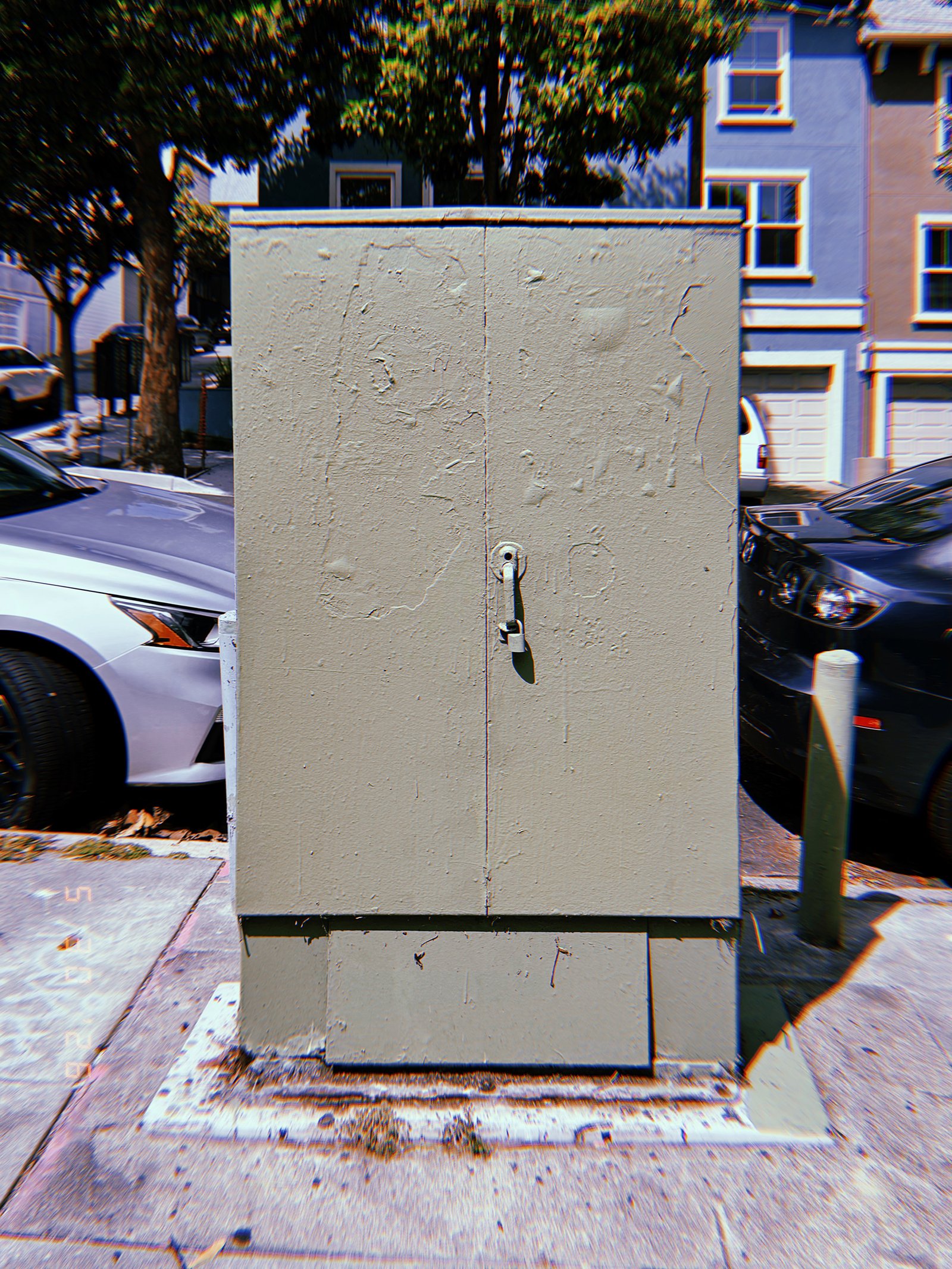 A light gray utility cabinet mounted on a concrete base along a San Francisco sidewalk, enclosing electrical or communications infrastructure behind locked metal doors.