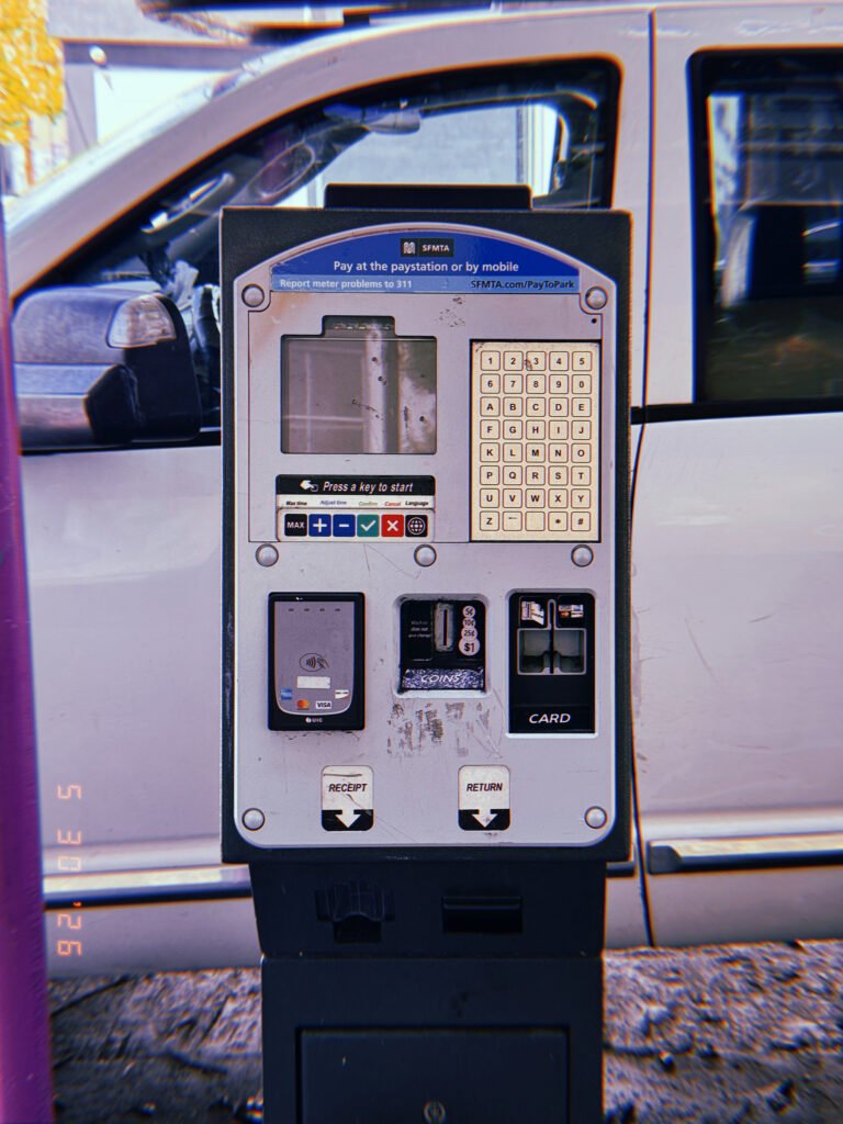 A San Francisco parking payment kiosk with digital display, keypad, contactless payment reader, coin slot, and card terminal installed beside a parked white van.