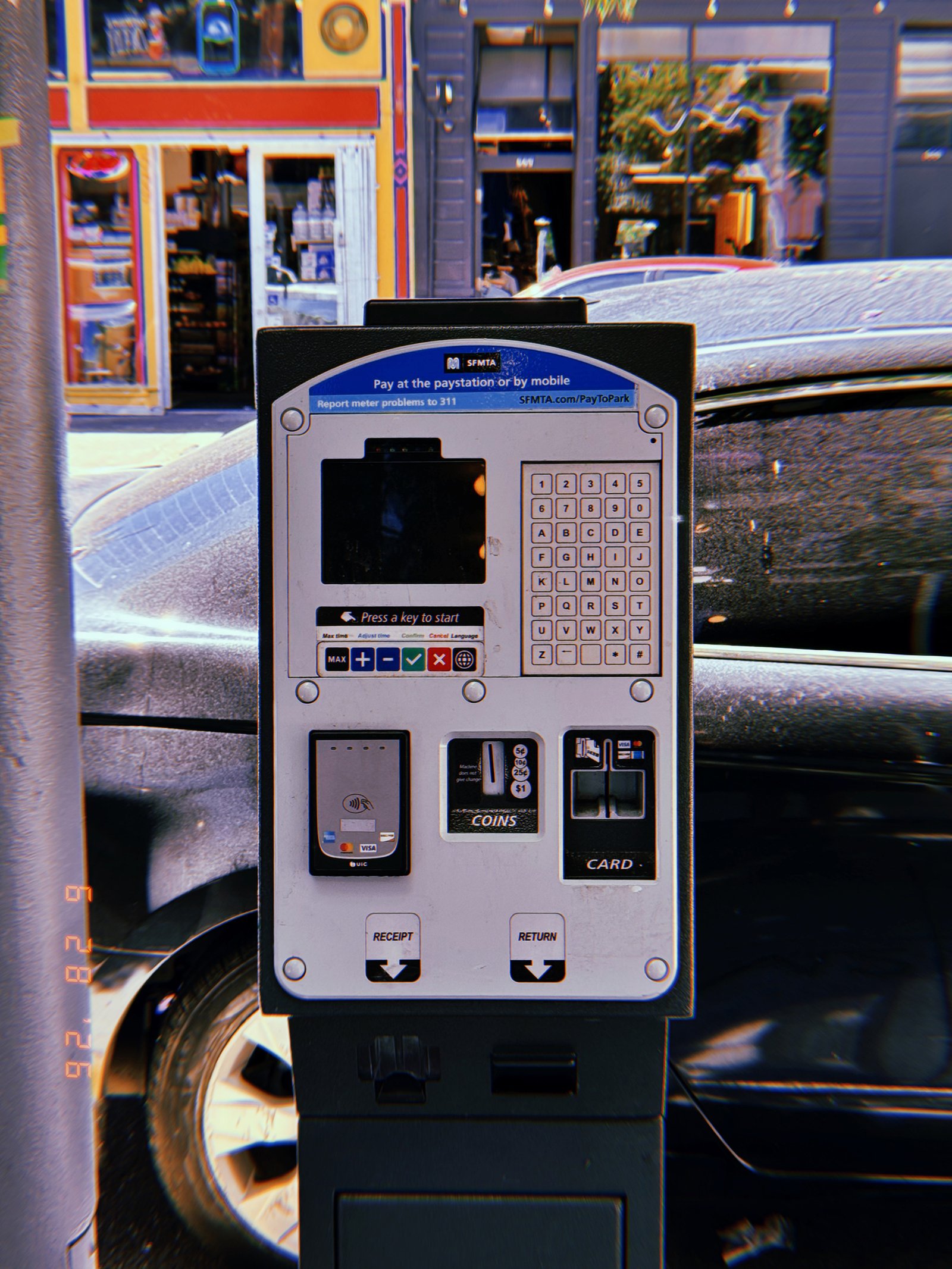 A San Francisco parking payment kiosk with touchscreen, keypad, contactless reader, coin slot, and card terminal installed along a commercial street with parked vehicles.