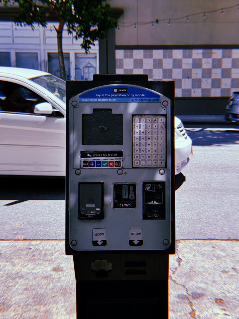 A San Francisco parking payment kiosk with touchscreen, keypad, contactless reader, coin slot, and card terminal standing beside a city street with passing traffic.