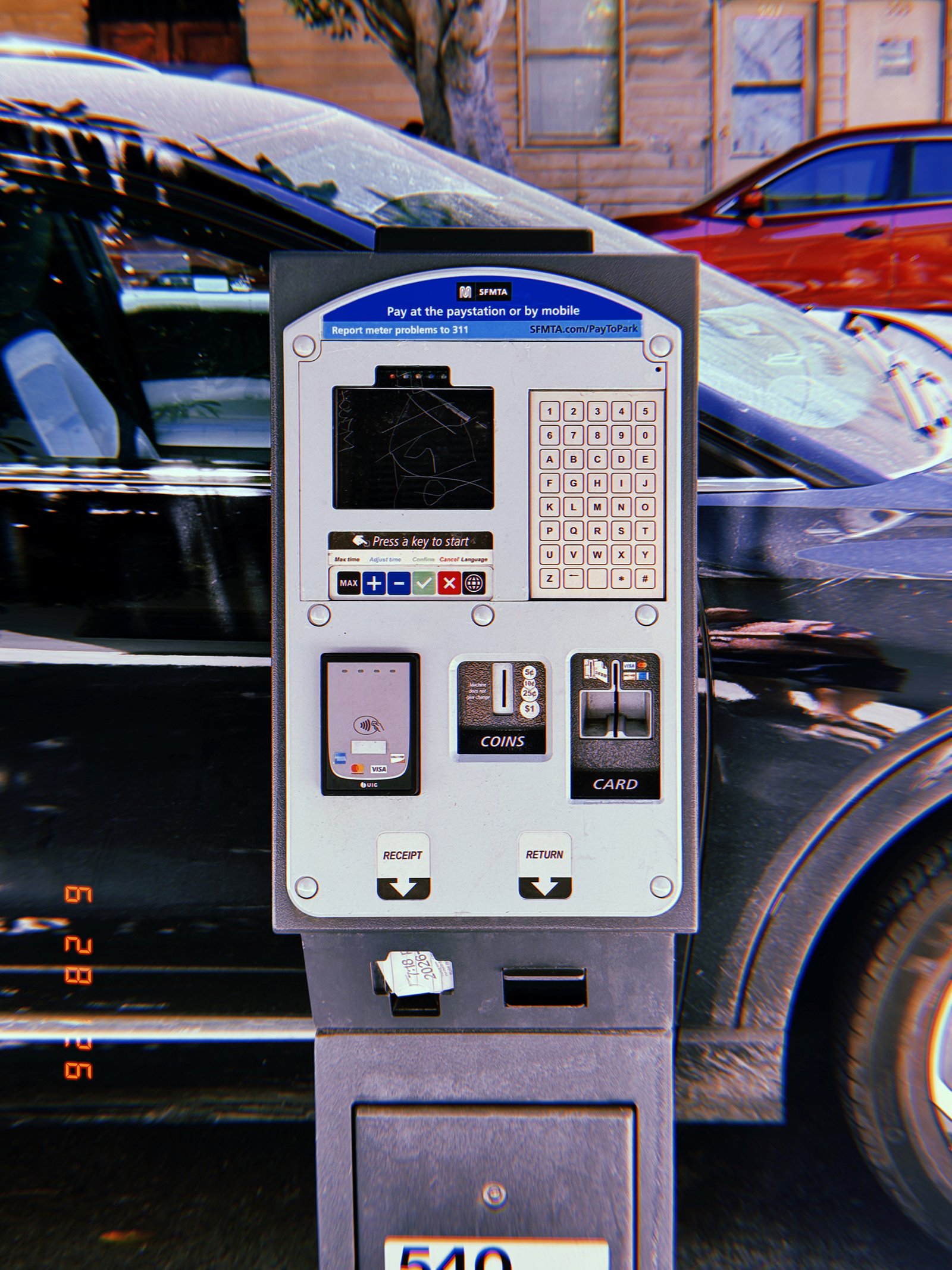 A San Francisco parking payment kiosk with keypad, card reader, coin slot, and receipt dispenser installed beside parked vehicles.