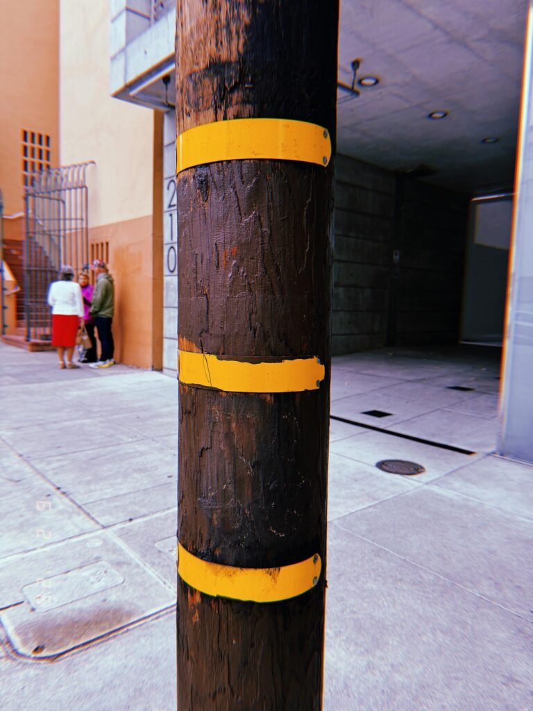 Wooden utility pole with three yellow identification bands on a San Francisco sidewalk.