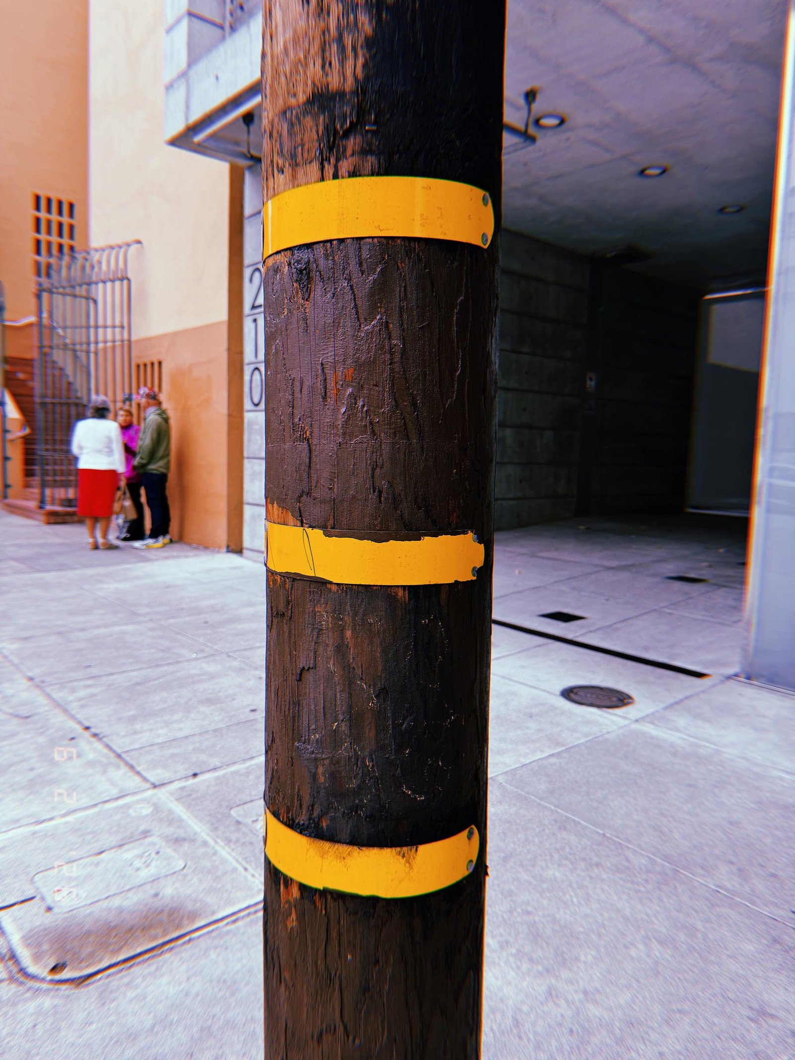 Wooden utility pole with three yellow identification bands on a San Francisco sidewalk.