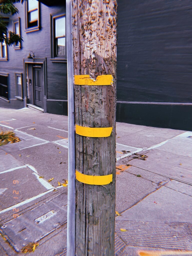 Weathered wooden utility pole with three yellow identification bands on a San Francisco sidewalk.