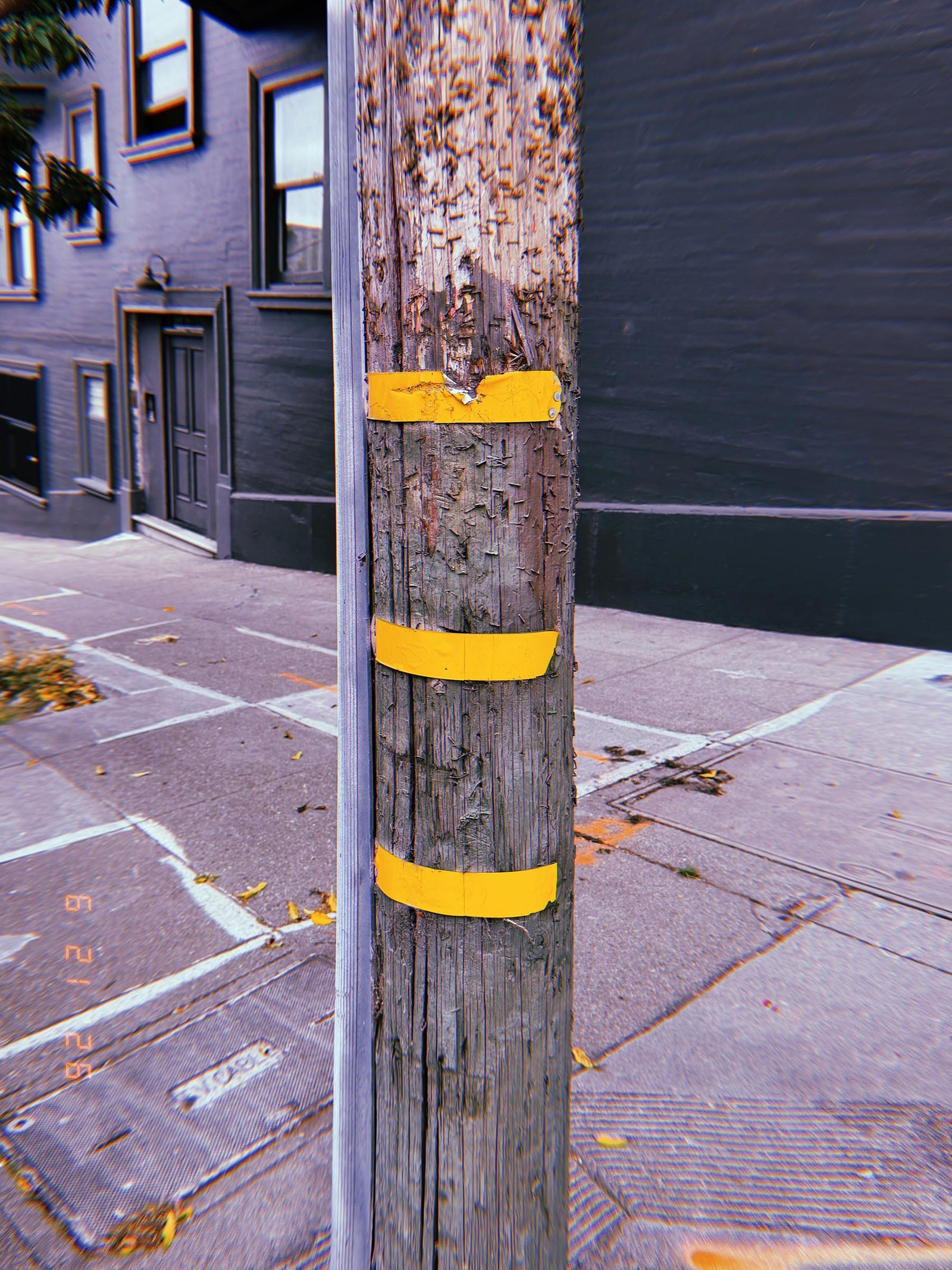 Weathered wooden utility pole with three yellow identification bands on a San Francisco sidewalk.