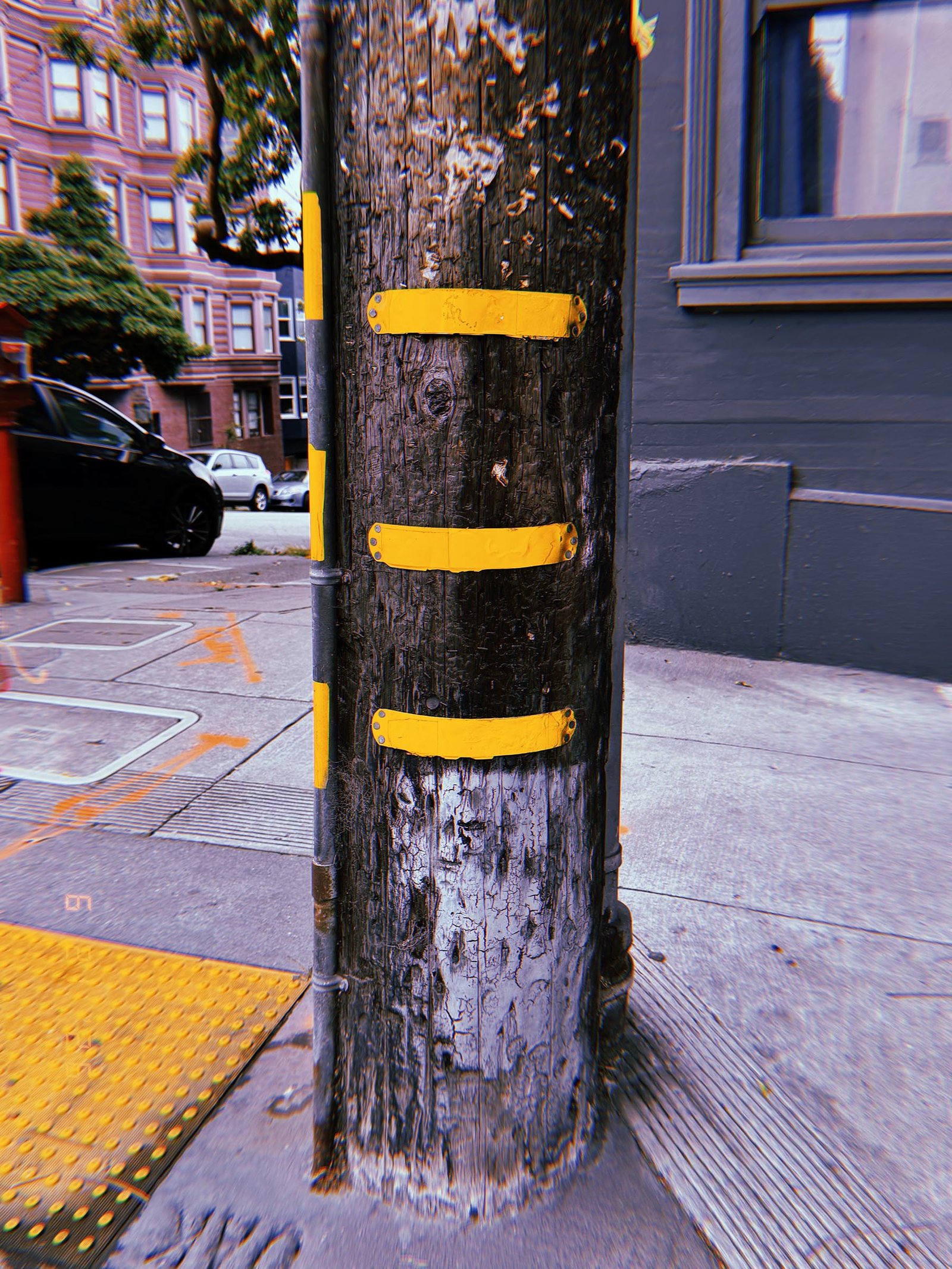 Wooden utility pole with three yellow identification bands at a San Francisco street corner.