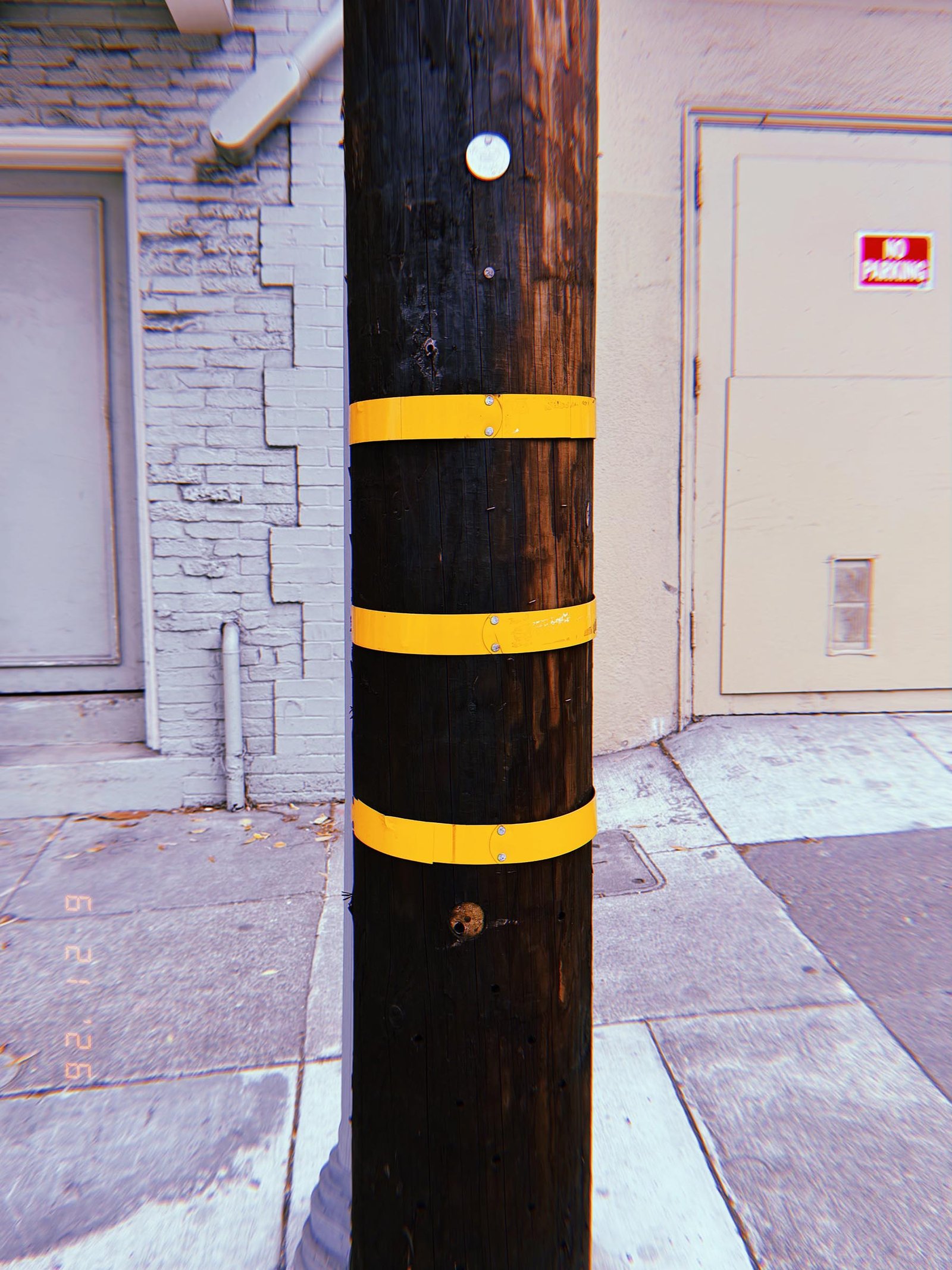 Dark wooden utility pole with three yellow identification bands on a San Francisco sidewalk.