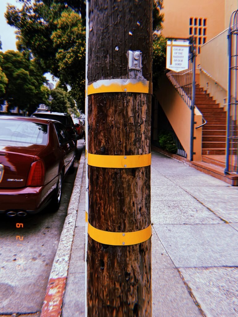 Wooden utility pole with three yellow identification bands along a residential San Francisco sidewalk.