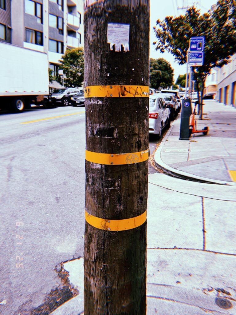 Wooden utility pole with three yellow identification bands marked with graffiti on a San Francisco street.