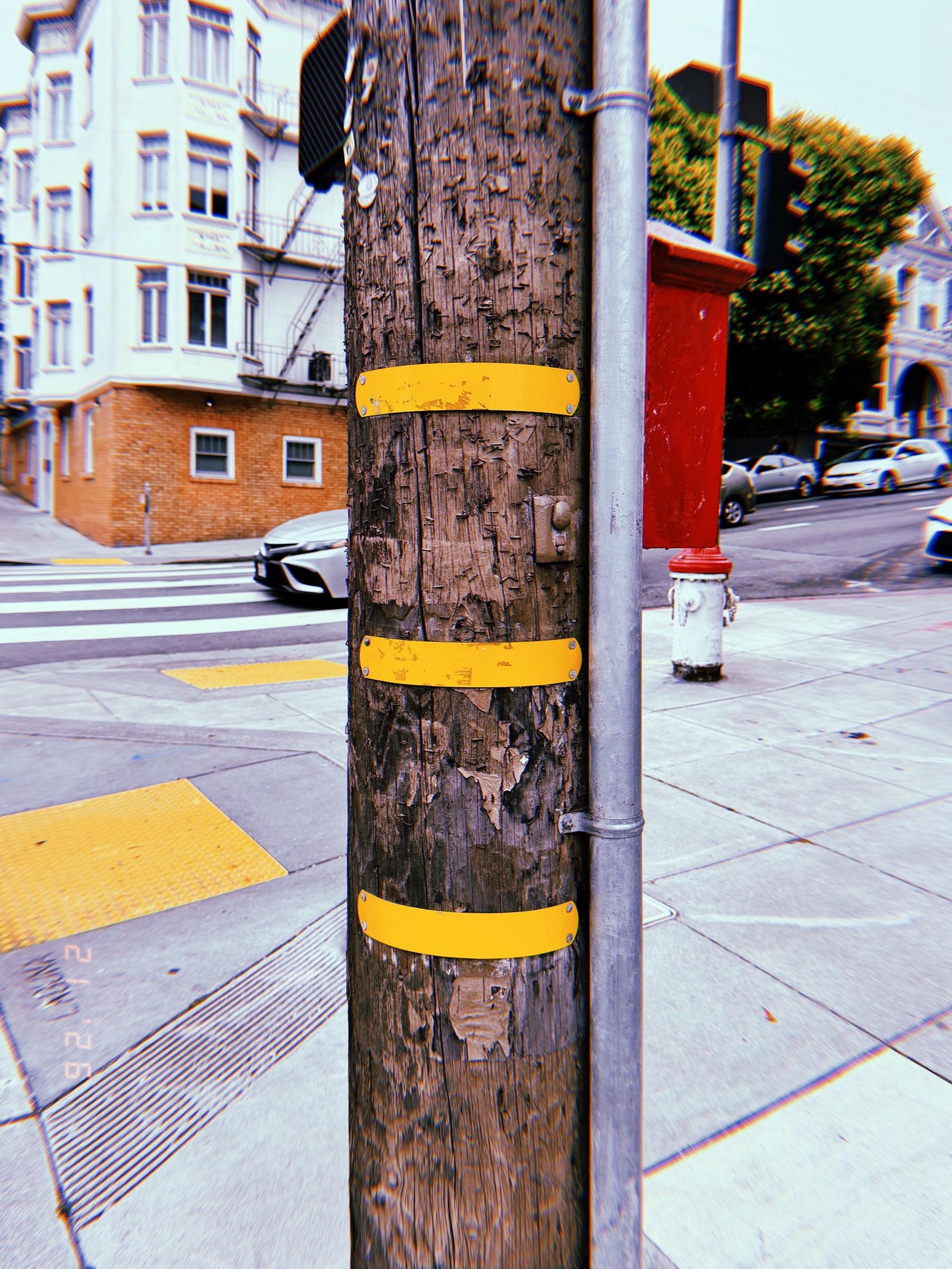 Wooden utility pole with three yellow identification bands at a San Francisco street intersection.