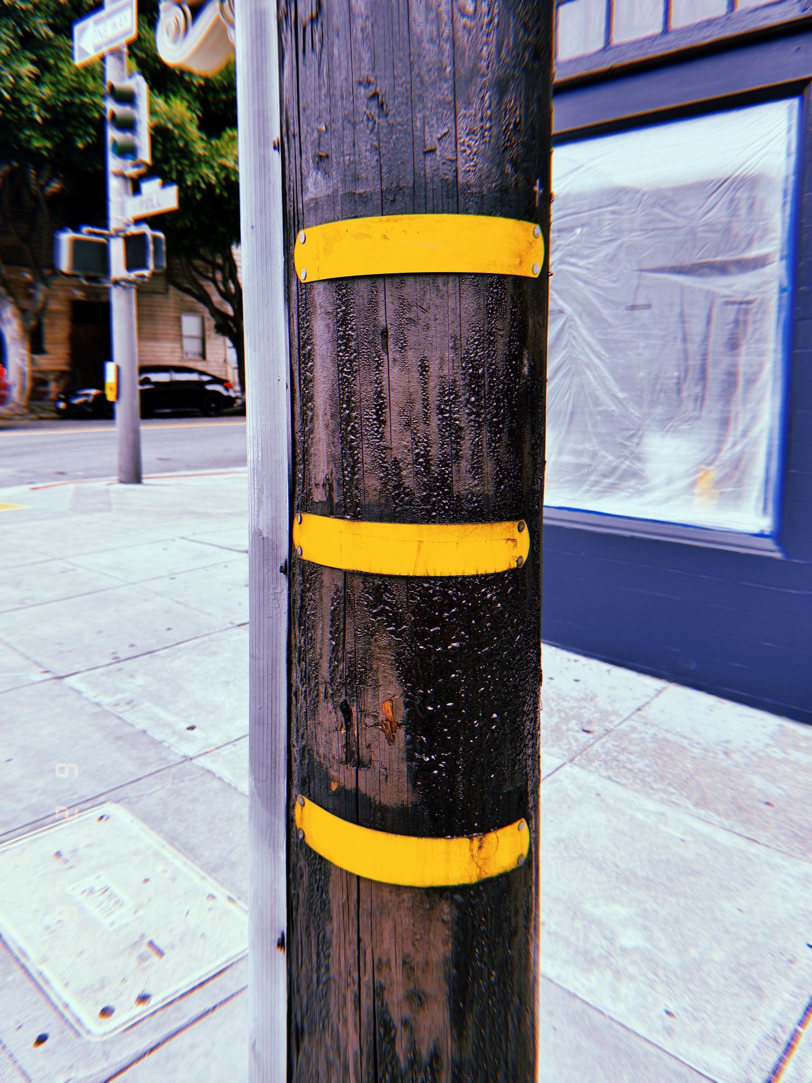 Wooden utility pole with three yellow identification bands on a San Francisco street corner.