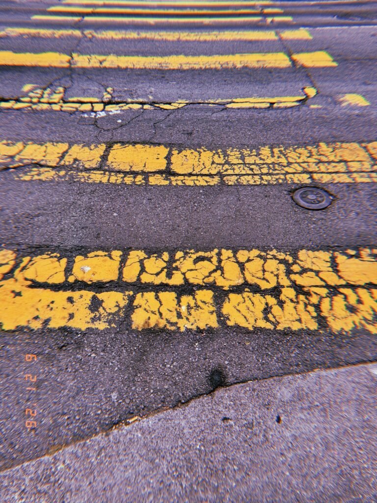 Cracked and fragmented yellow crosswalk stripes across worn asphalt in San Francisco.