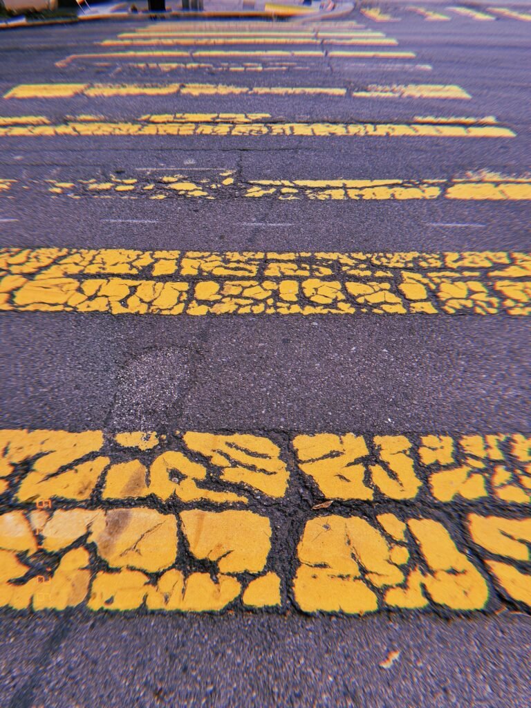 Heavily cracked yellow crosswalk stripes extending across dark asphalt in San Francisco.