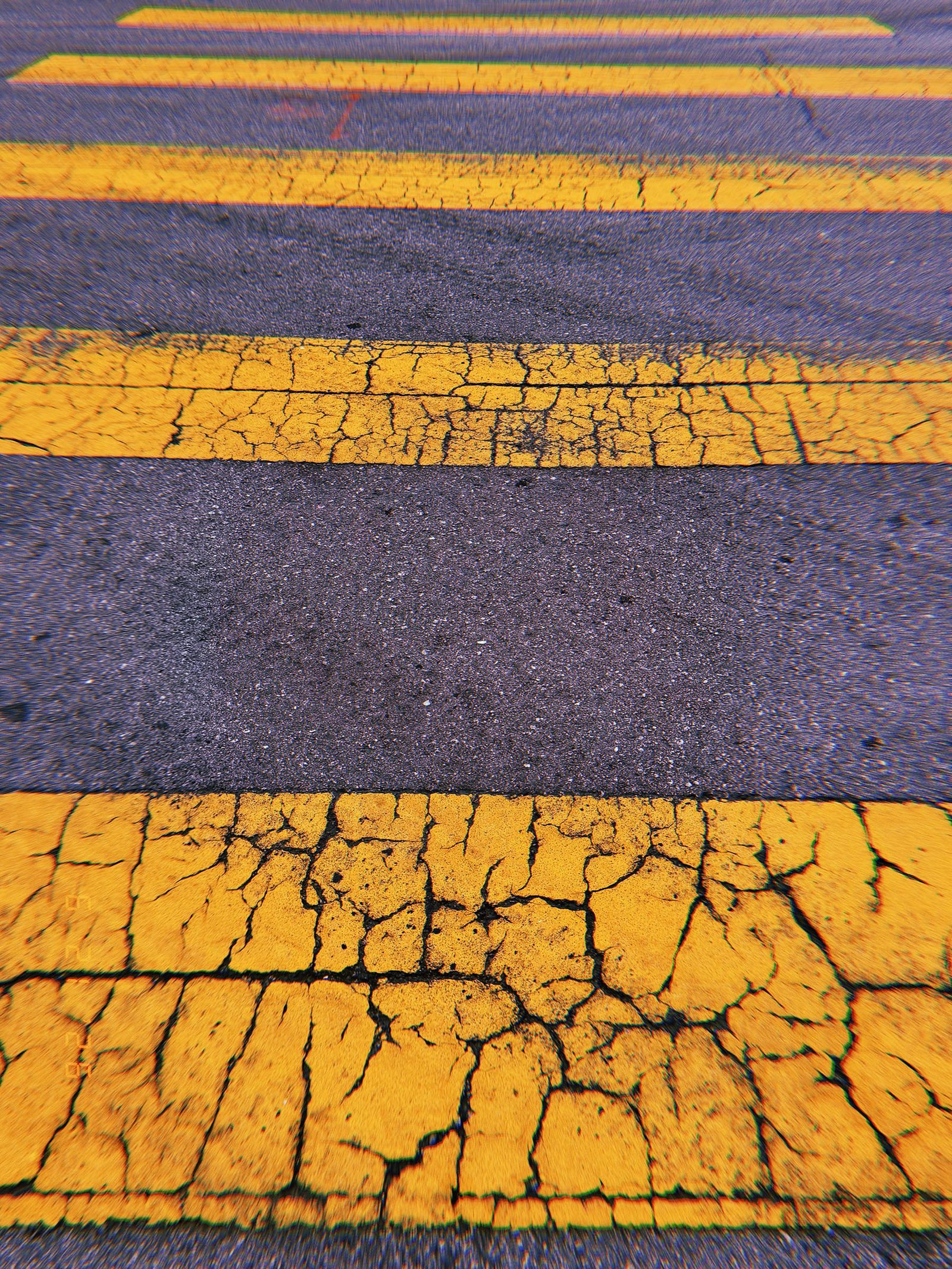 Cracked yellow crosswalk stripes extending across dark asphalt in San Francisco.