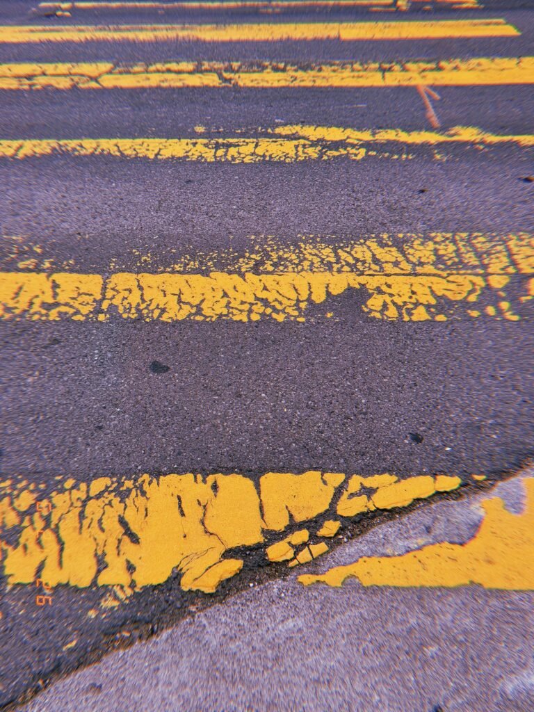 Worn and fragmented yellow crosswalk stripes across dark asphalt in San Francisco.