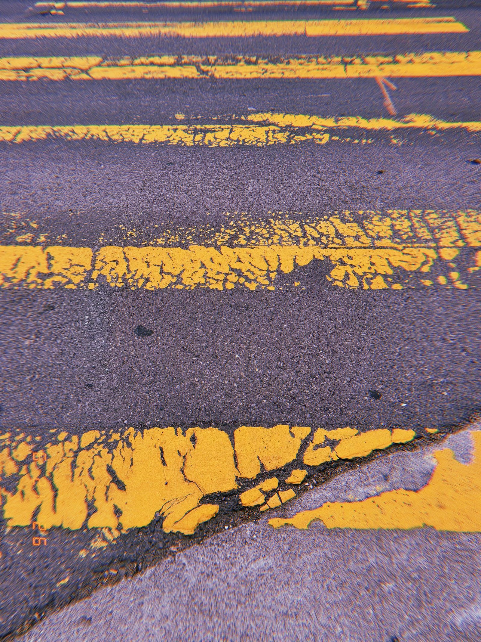 Worn and fragmented yellow crosswalk stripes across dark asphalt in San Francisco.