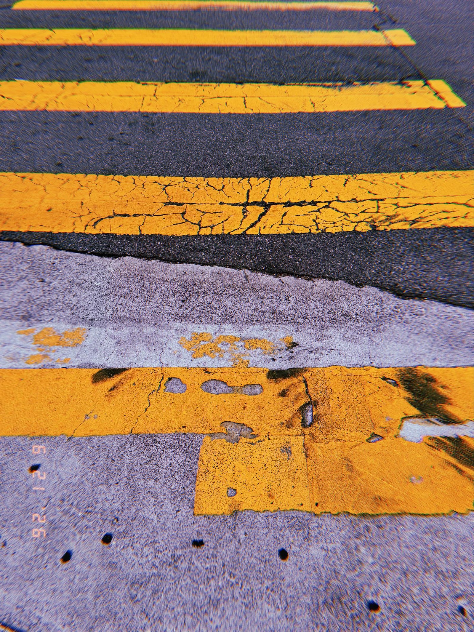 Cracked yellow crosswalk stripes meeting a worn concrete street surface in San Francisco.