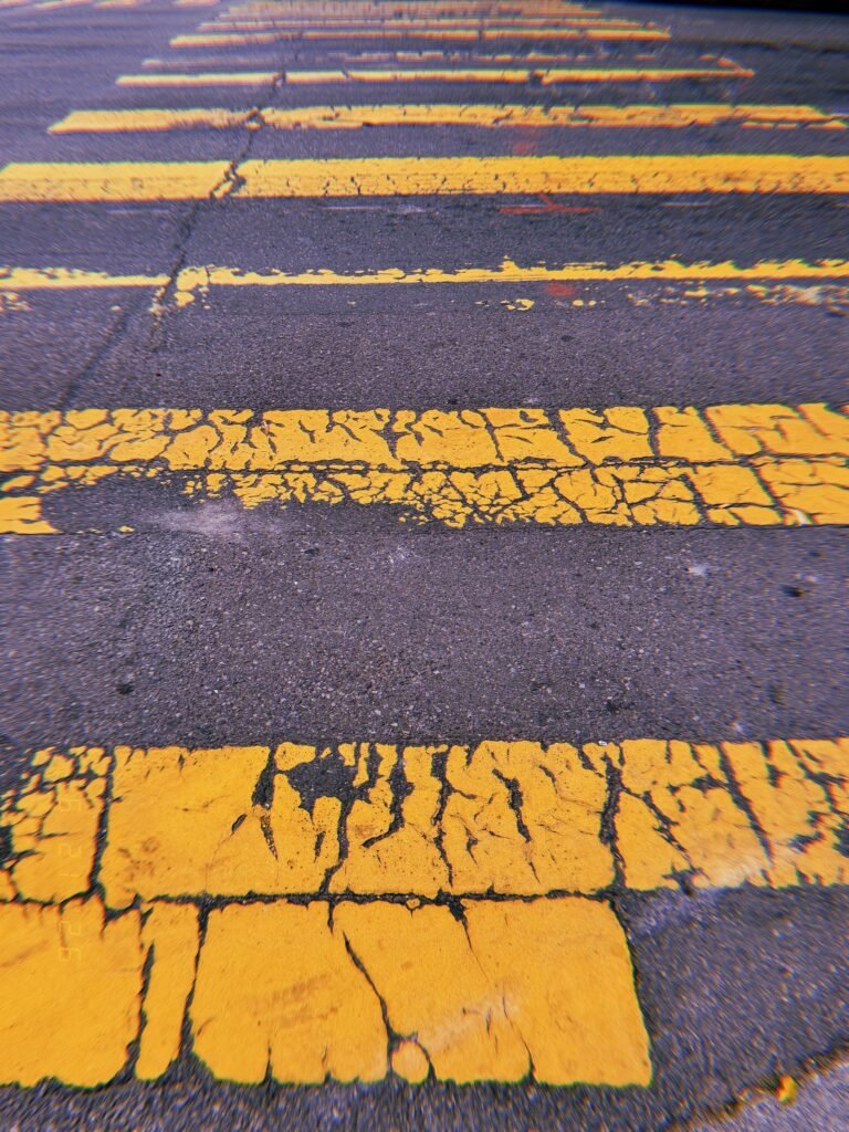 Heavily cracked yellow crosswalk stripes across worn asphalt in San Francisco.