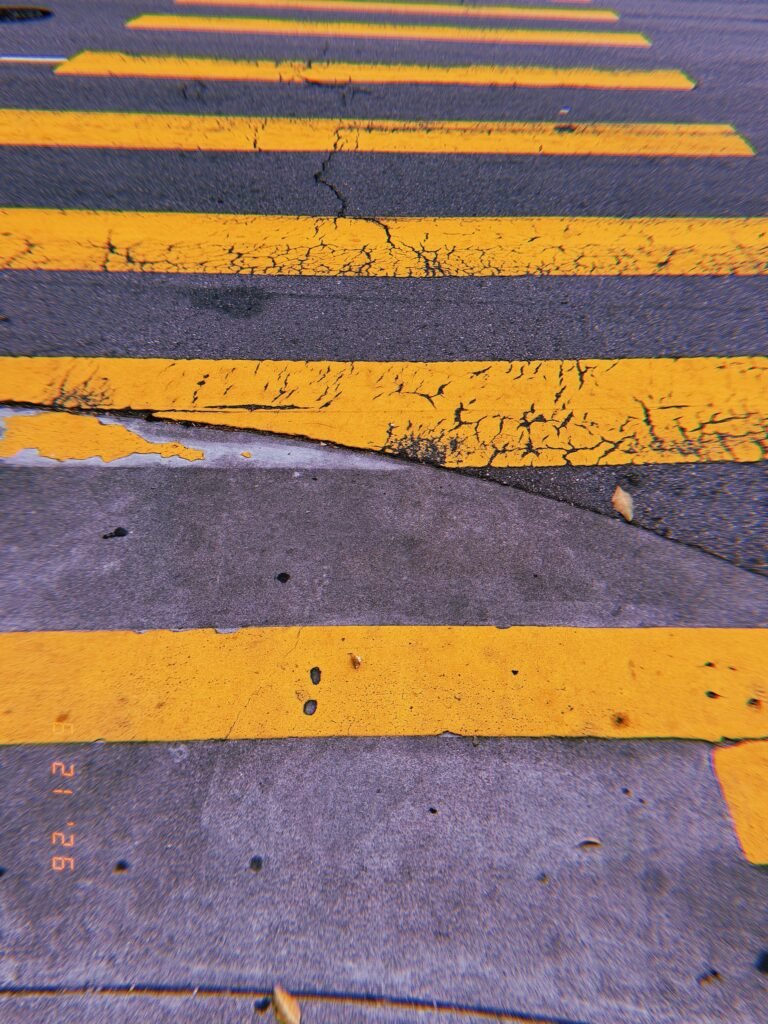 Cracked yellow crosswalk stripes extending across worn asphalt in San Francisco.