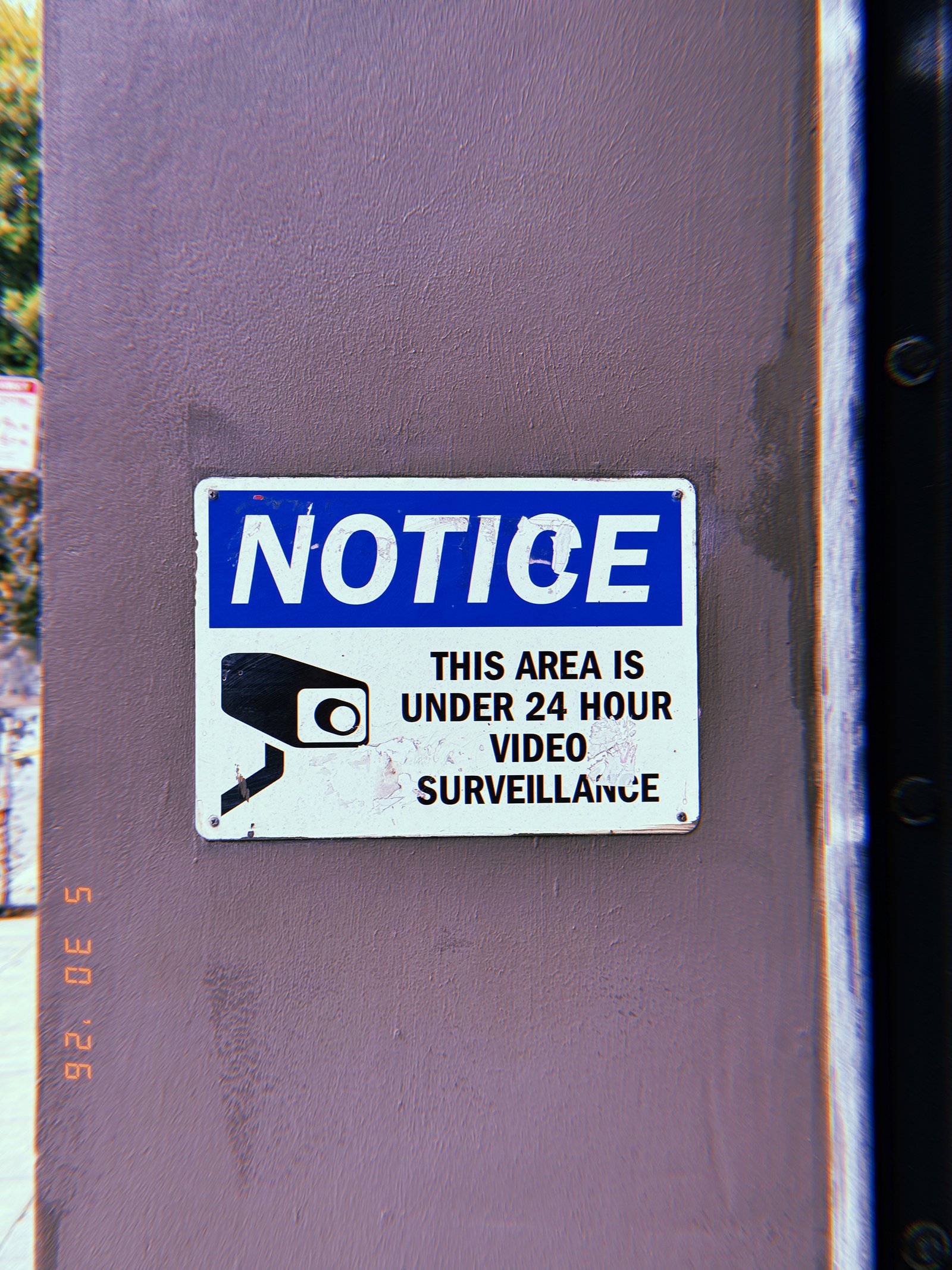 Notice sign stating the area is under 24-hour video surveillance, with a security camera graphic, mounted on an exterior wall in San Francisco.