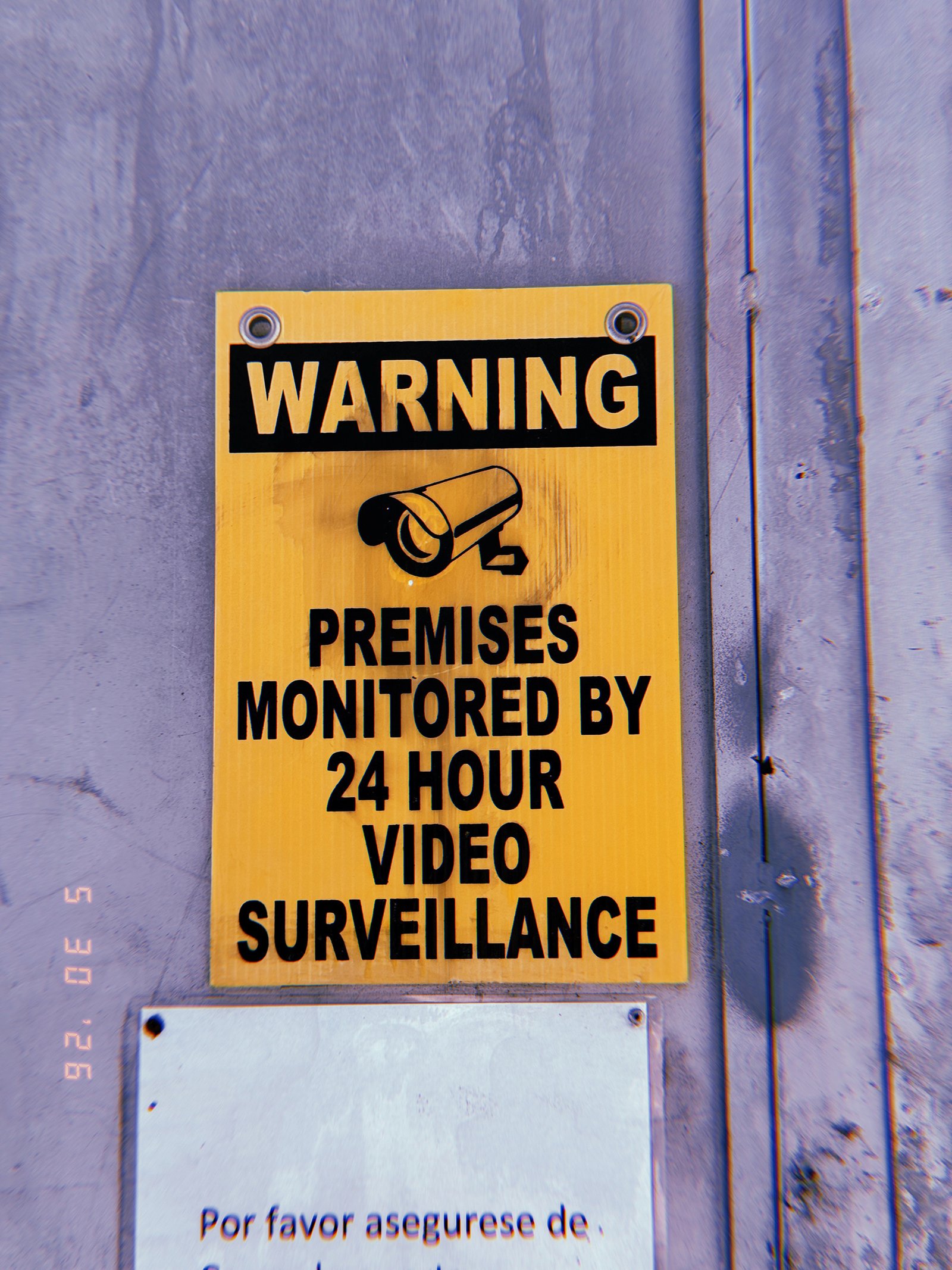 Yellow warning sign stating premises are monitored by 24-hour video surveillance on a gray wall in San Francisco.