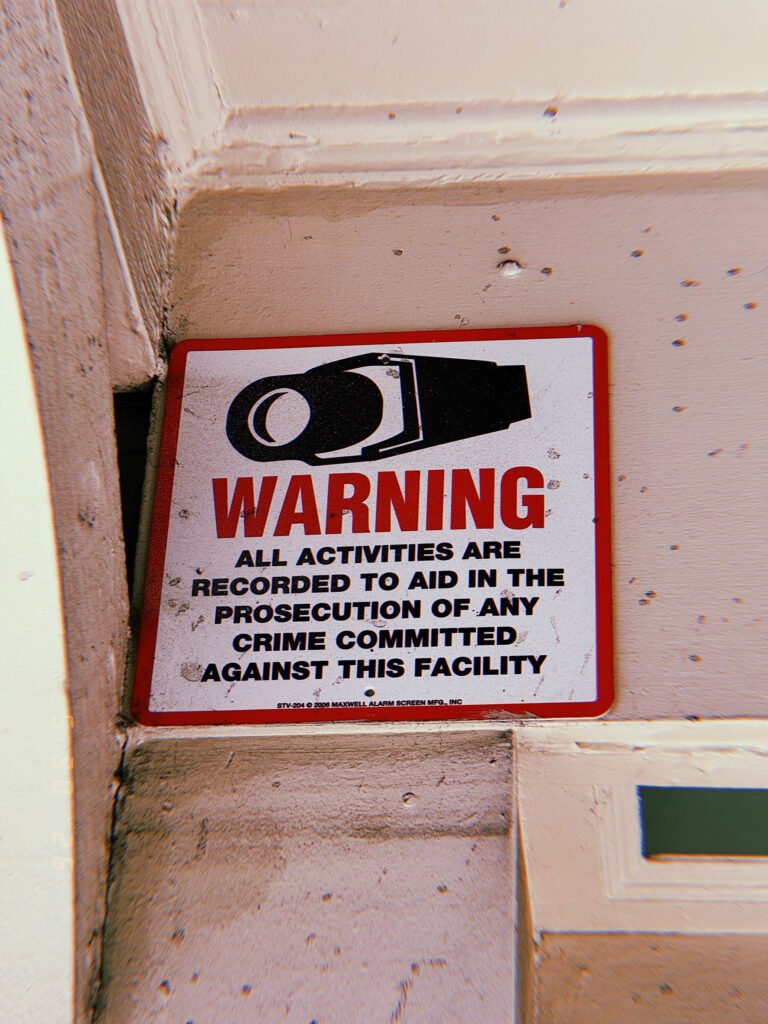 Surveillance warning sign with a security camera symbol mounted on an exterior wall in San Francisco.