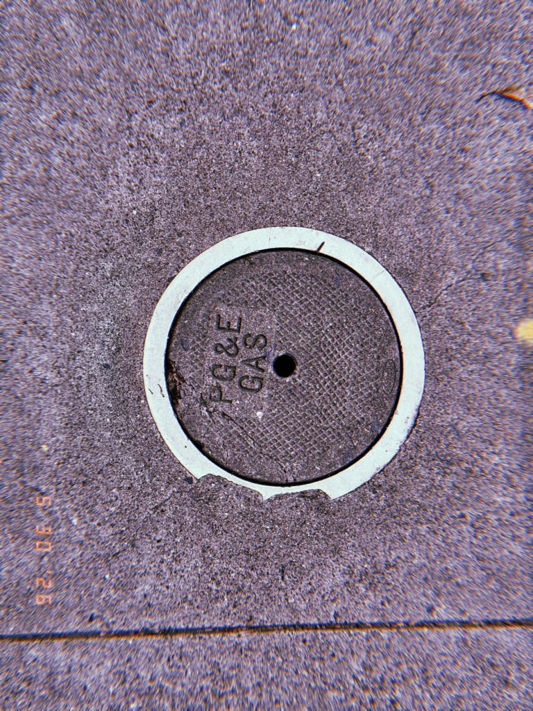 Round PG&E gas utility cover embedded in a textured San Francisco sidewalk, with a pale circular border and central access hole.