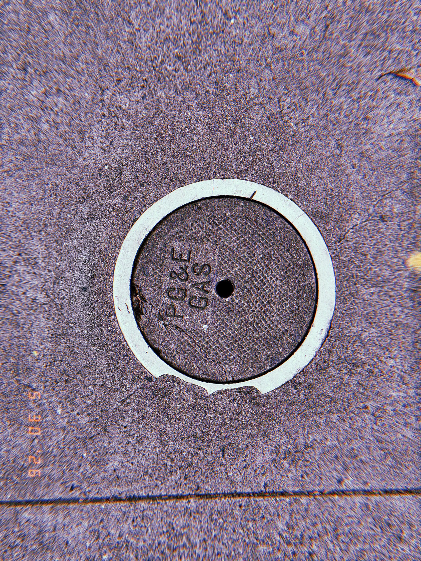 Round PG&E gas utility cover embedded in a textured San Francisco sidewalk, with a pale circular border and central access hole.