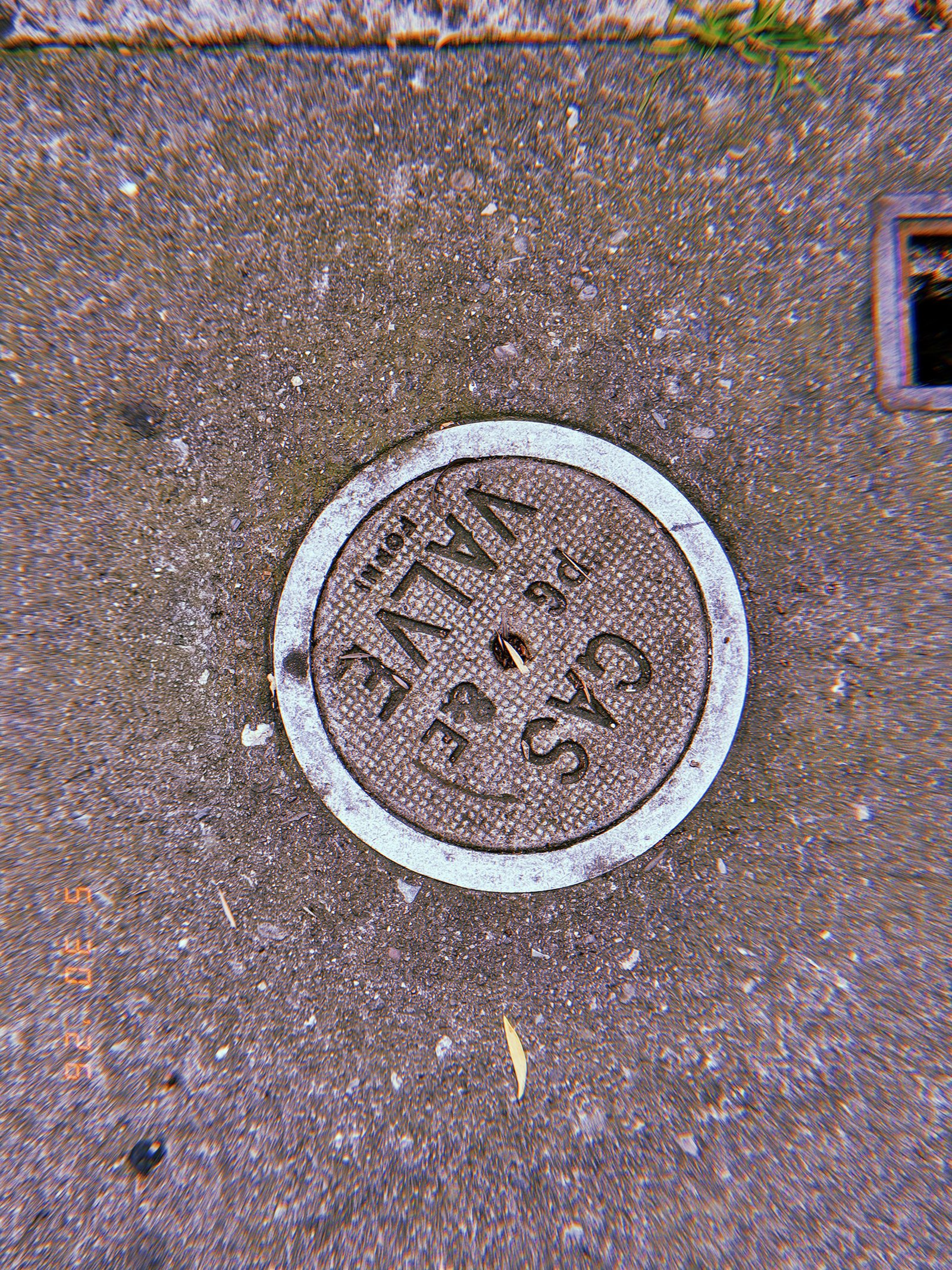 Round metal gas valve cover marked “VALVE GAS” embedded in a textured San Francisco sidewalk and surrounded by a pale circular border.