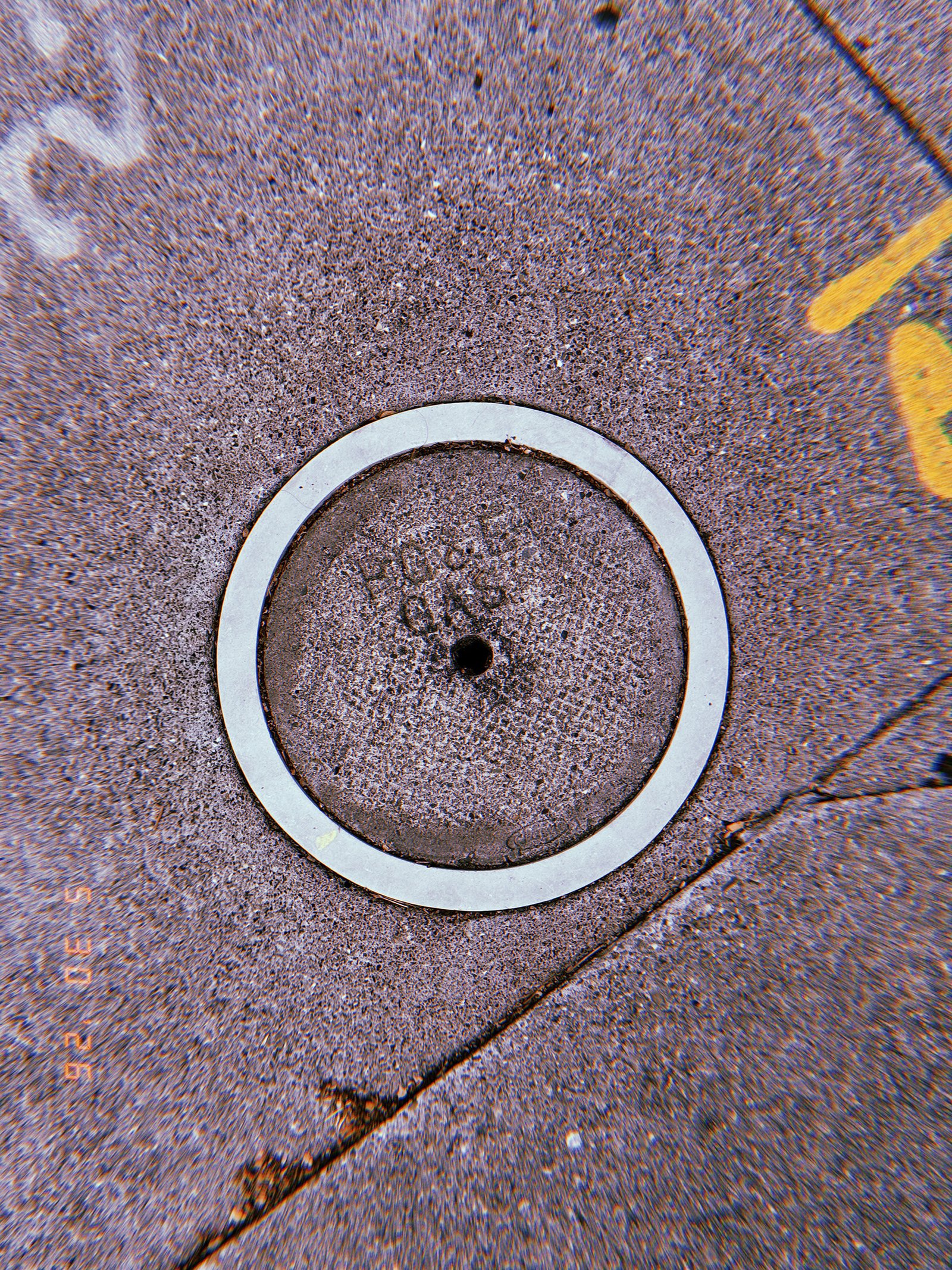 Round metal gas utility cover embedded in a textured San Francisco sidewalk, surrounded by a pale circular border and yellow utility markings.
