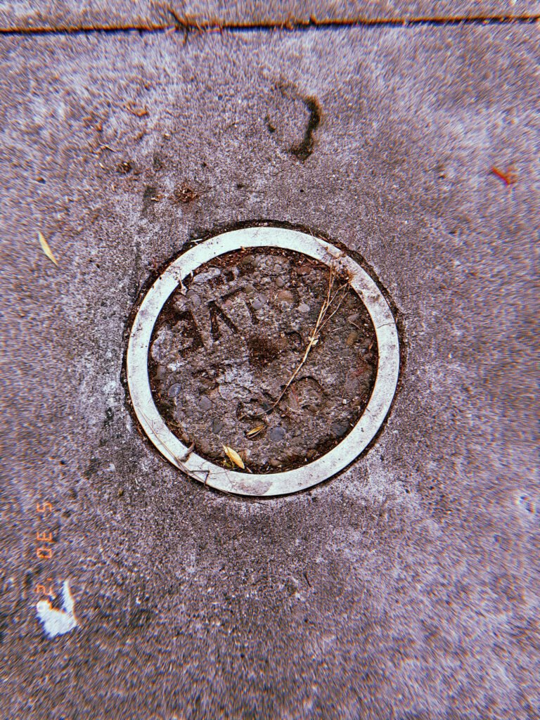 Circular gas utility access point embedded in a textured San Francisco sidewalk, filled with rough concrete and surrounded by a worn pale ring.