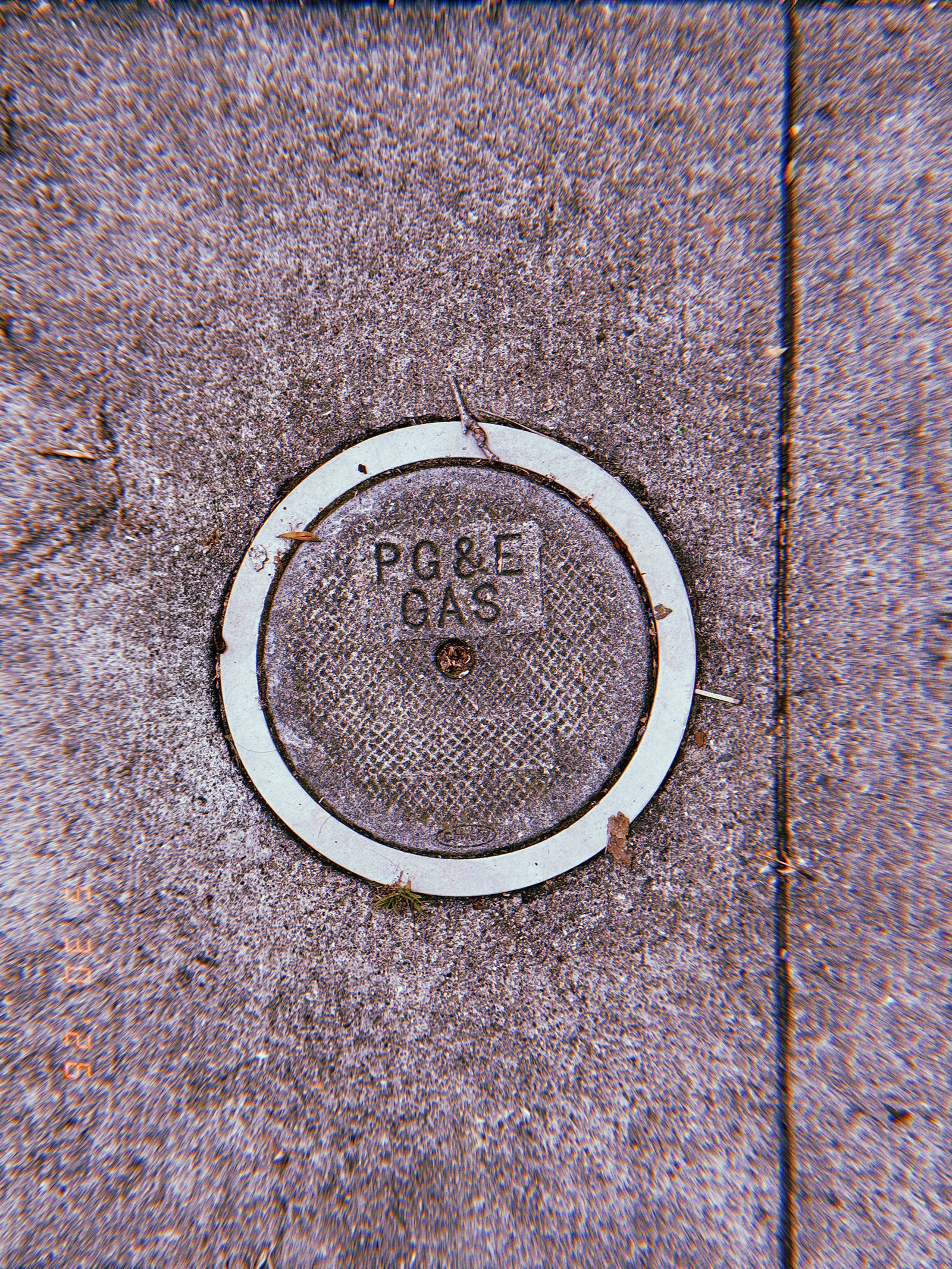 Round PG&E gas utility cover embedded in a textured San Francisco sidewalk, surrounded by a pale circular border and small street debris.