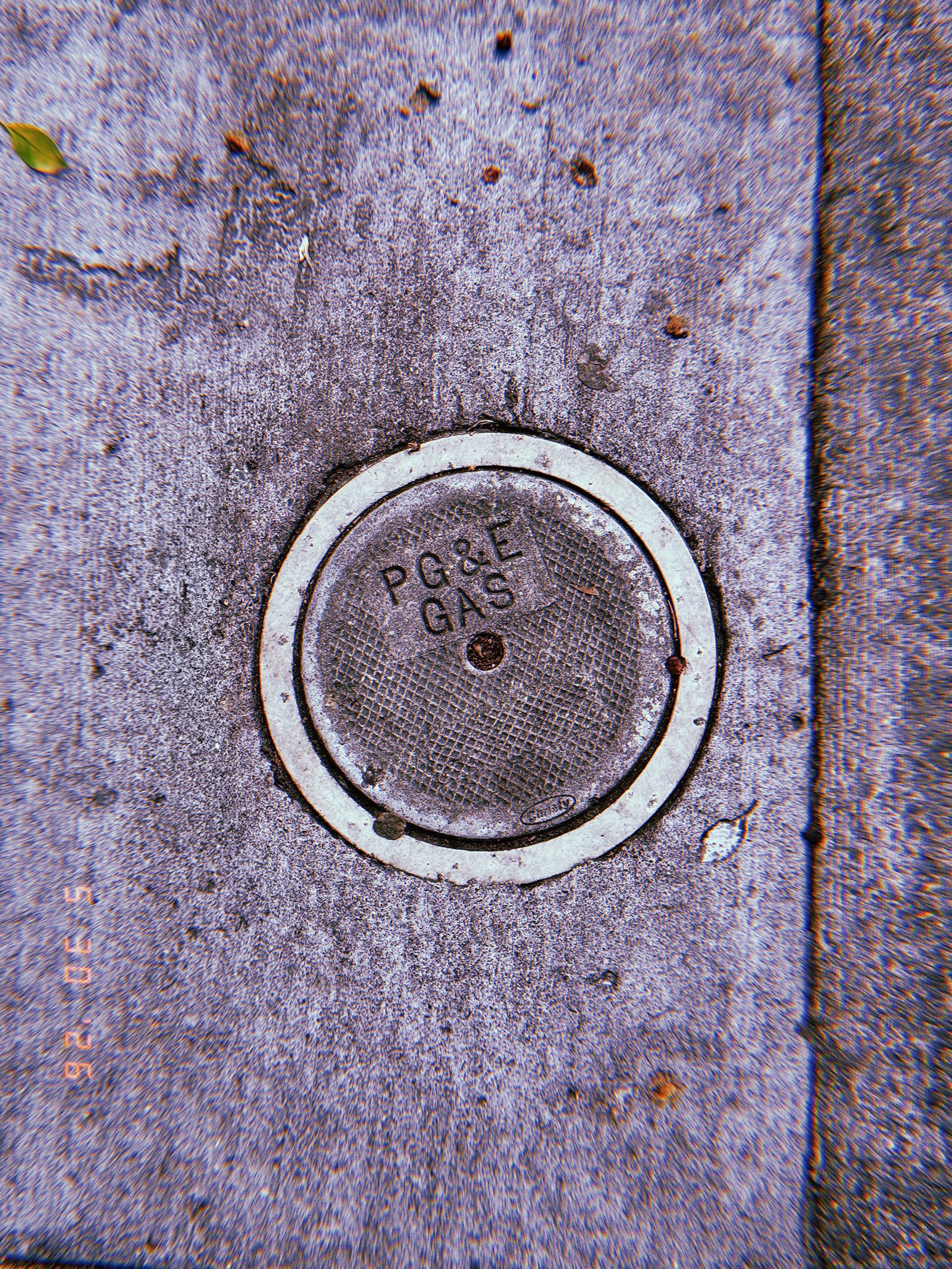 Round PG&E gas utility cover embedded in a textured San Francisco sidewalk, showing the marked access point to underground gas infrastructure.