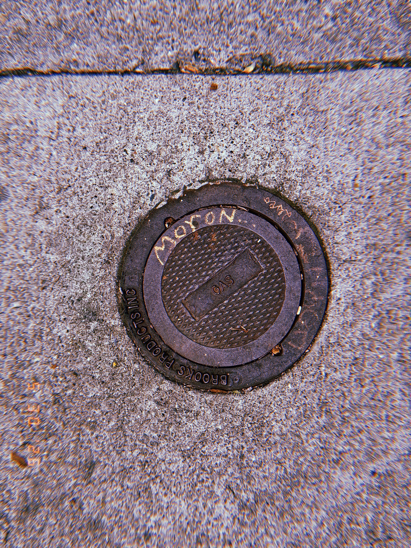 Round metal gas utility valve cover embedded in a concrete San Francisco sidewalk, marked “GAS” and surrounded by worn pavement.