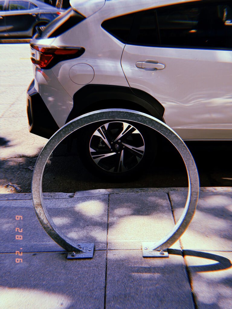 Circular galvanized metal bicycle rack mounted on a San Francisco sidewalk, positioned directly in front of a parked silver SUV.