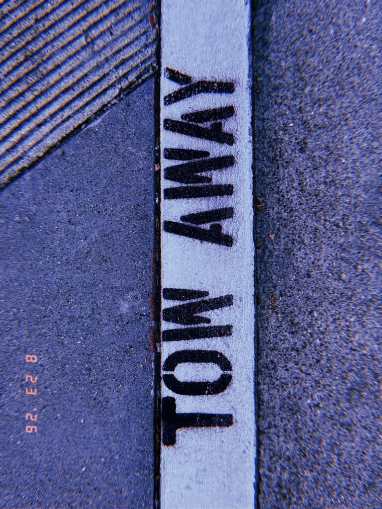 Black “TOW AWAY” lettering painted on a white curb between the sidewalk and street.