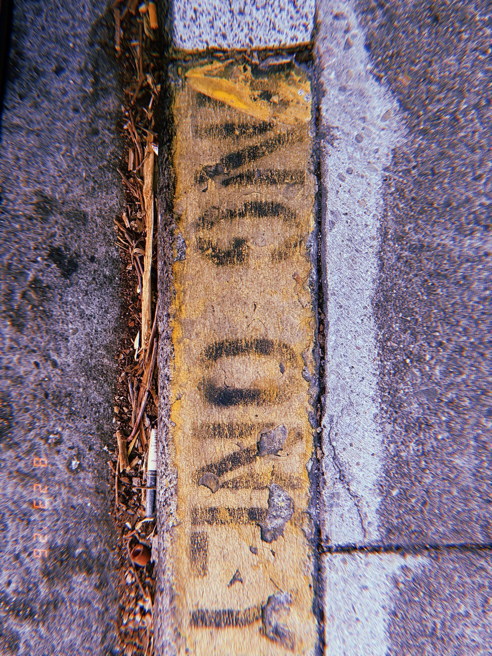 Faded black curb markings painted over a worn yellow curb beside a San Francisco sidewalk.