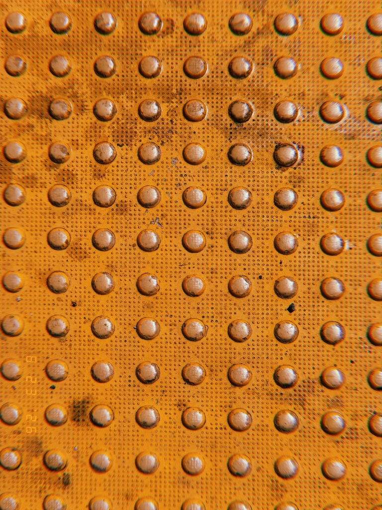 Close-up of an orange tactile warning surface with a repeating grid of worn raised domes.