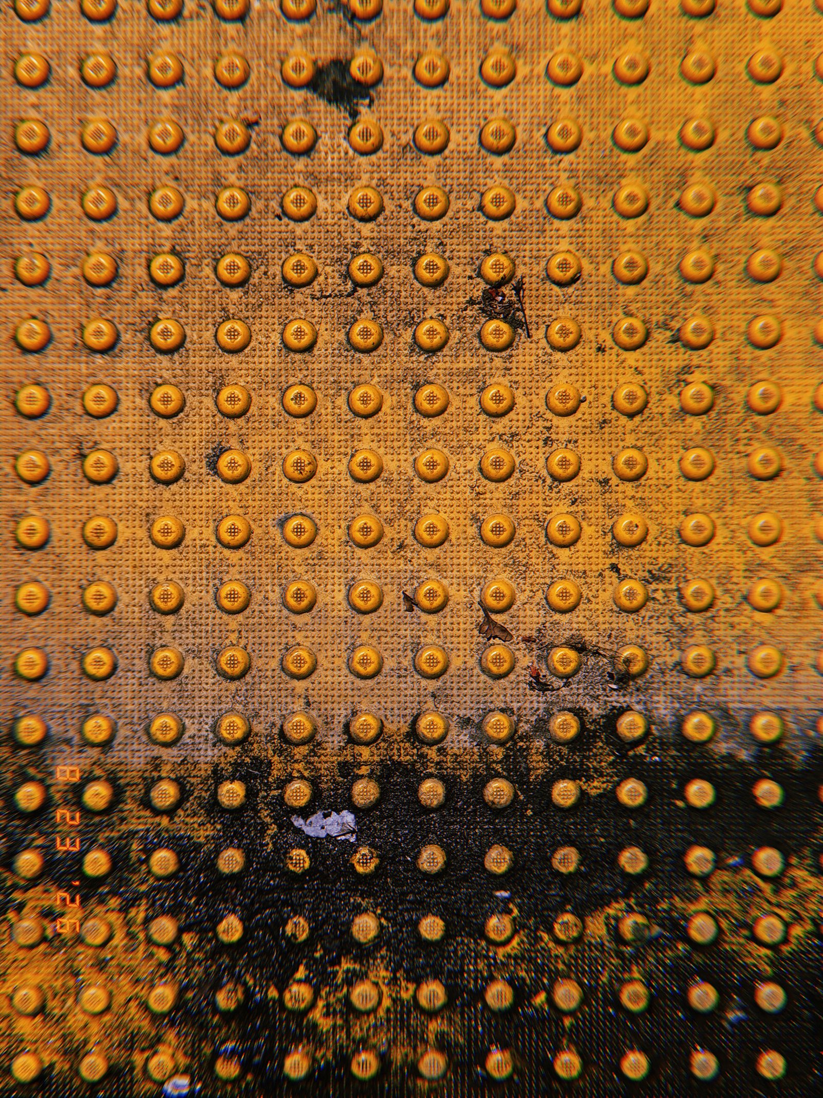 Worn orange tactile paving with a grid of raised truncated domes, dark stains, debris, and surface damage.