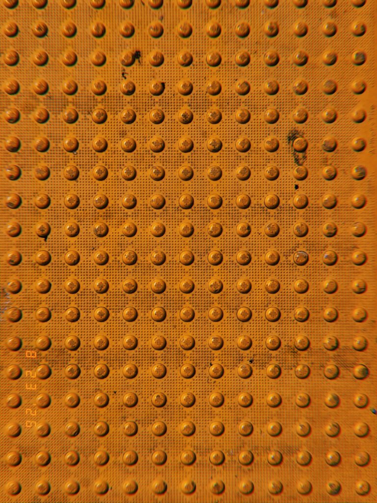 Orange tactile paving with a uniform grid of raised truncated domes and scattered signs of wear.