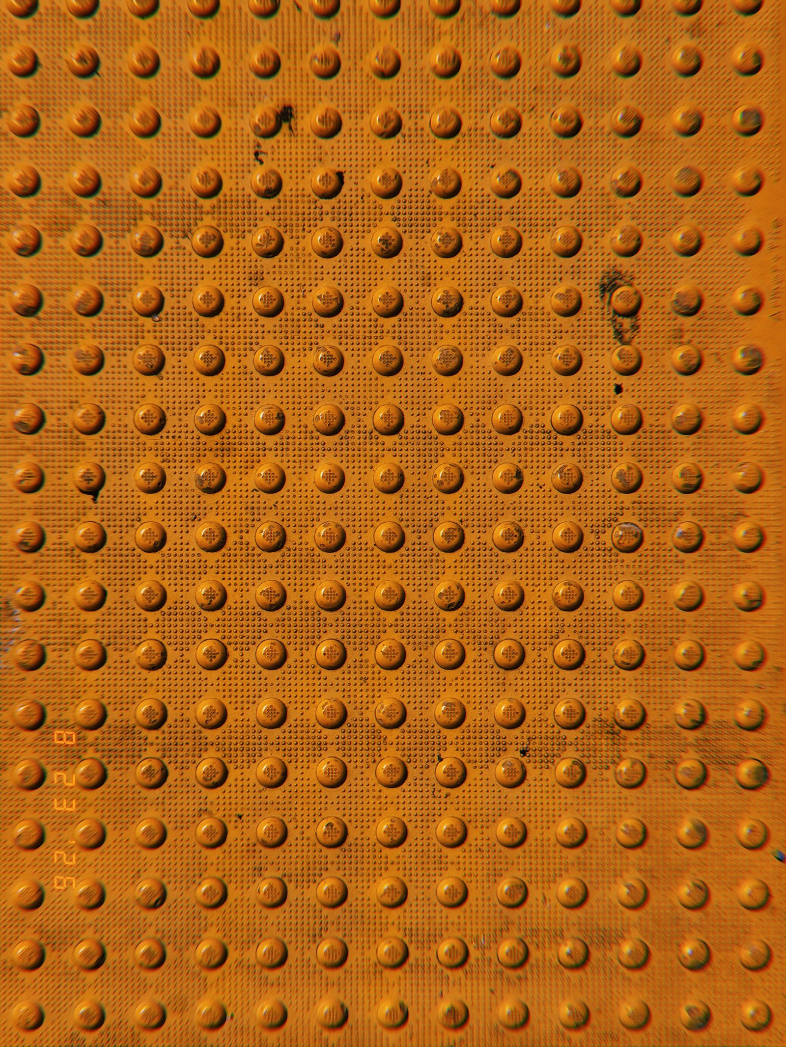 Orange tactile paving with a uniform grid of raised truncated domes and scattered signs of wear.