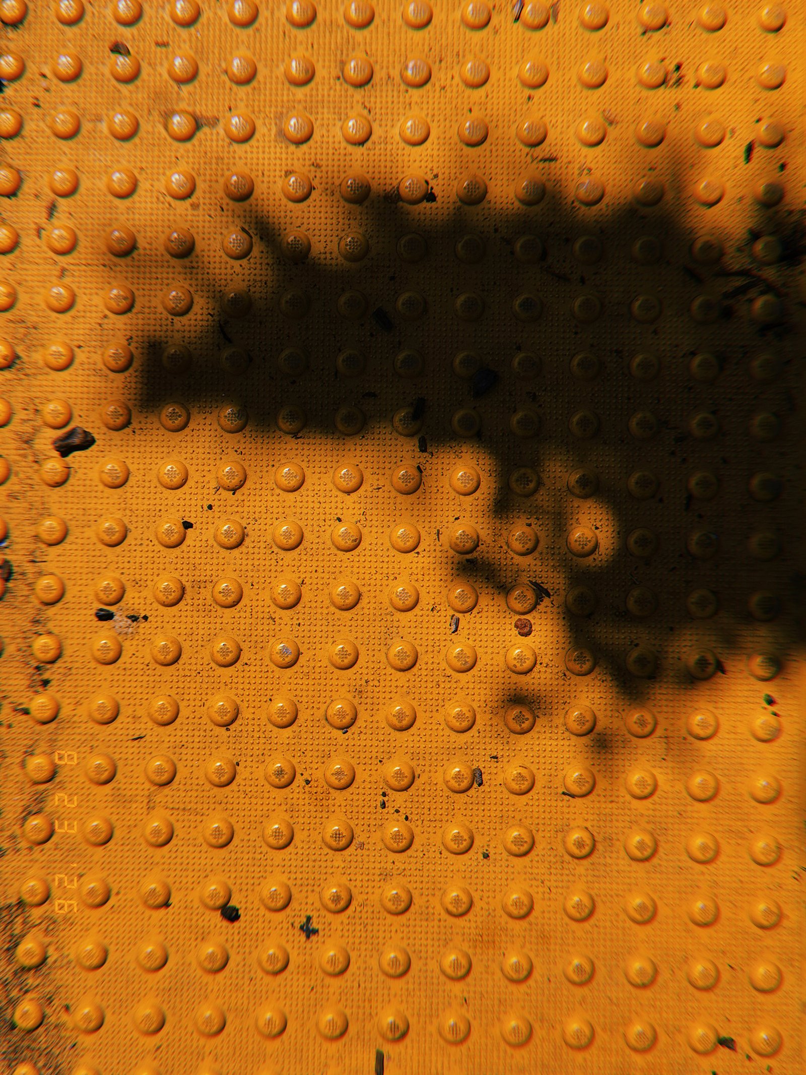 Orange tactile paving with rows of raised truncated domes partially covered by a large tree shadow.