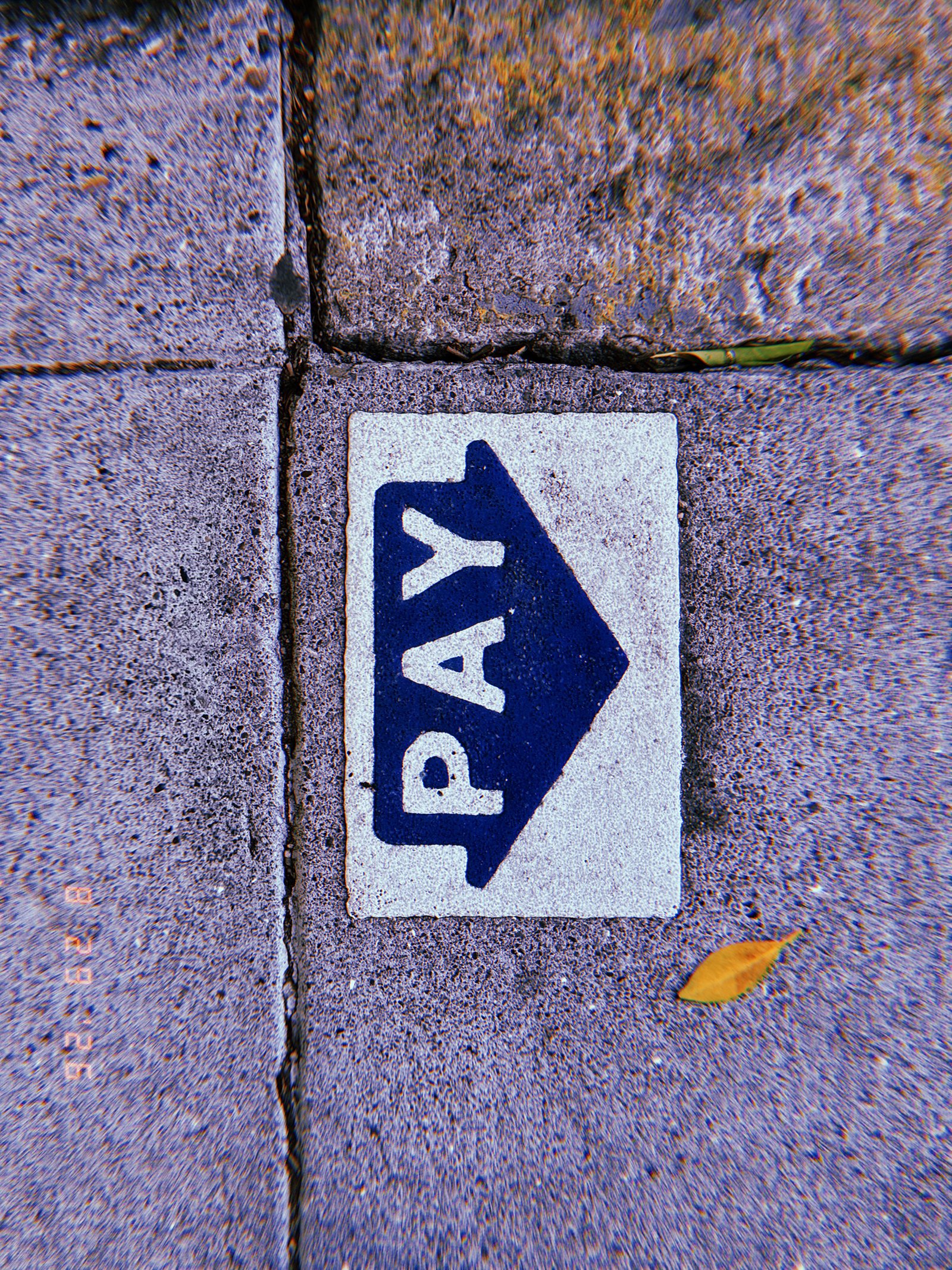 Blue PAY arrow marking embedded in a concrete sidewalk, indicating the direction of a parking payment point.