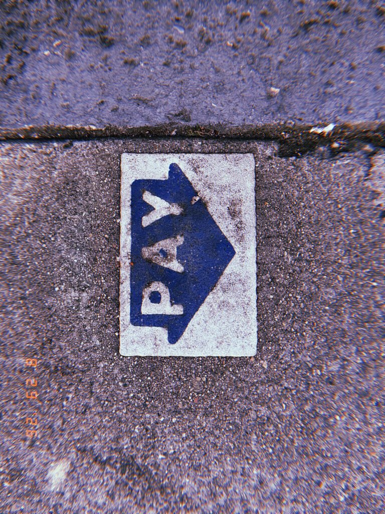 Worn blue PAY arrow marking embedded in a concrete sidewalk, directing pedestrians toward a parking payment point.