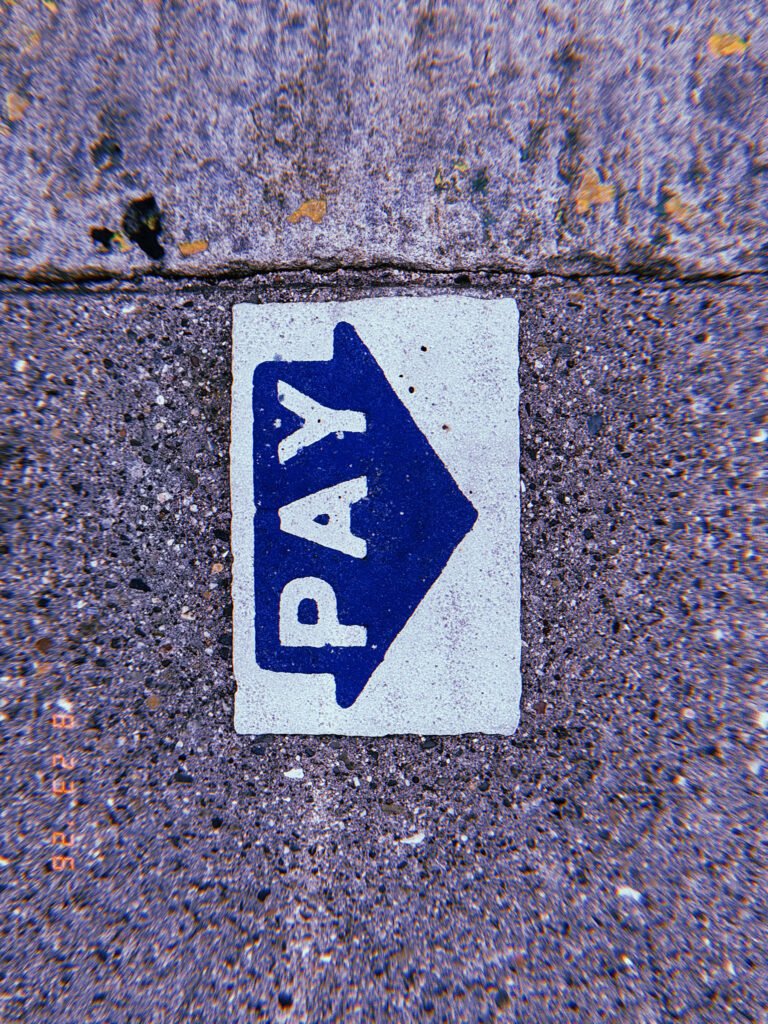 Blue PAY arrow marking embedded in a worn concrete sidewalk, indicating the direction of a parking payment point.