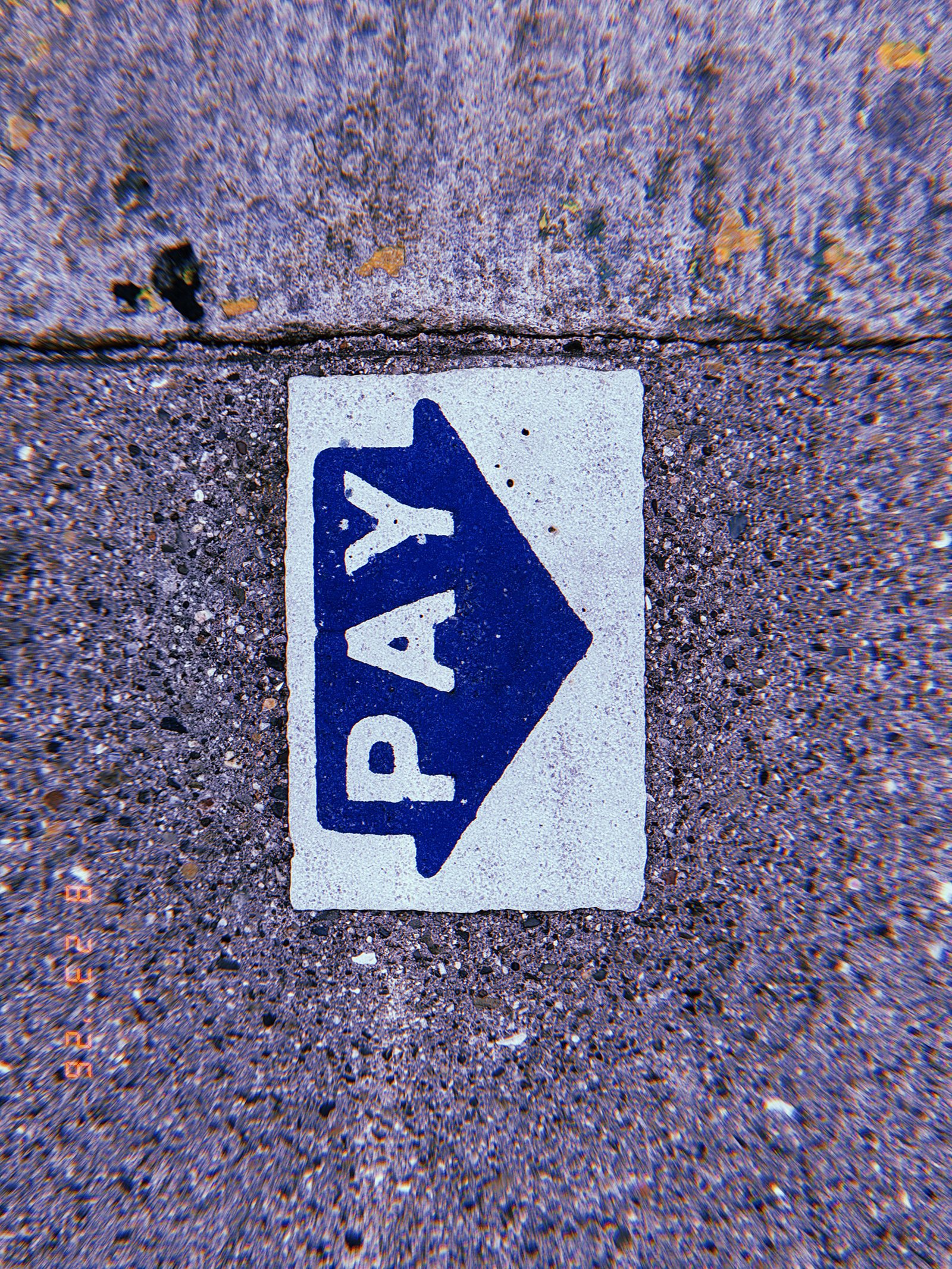 Blue PAY arrow marking embedded in a worn concrete sidewalk, indicating the direction of a parking payment point.
