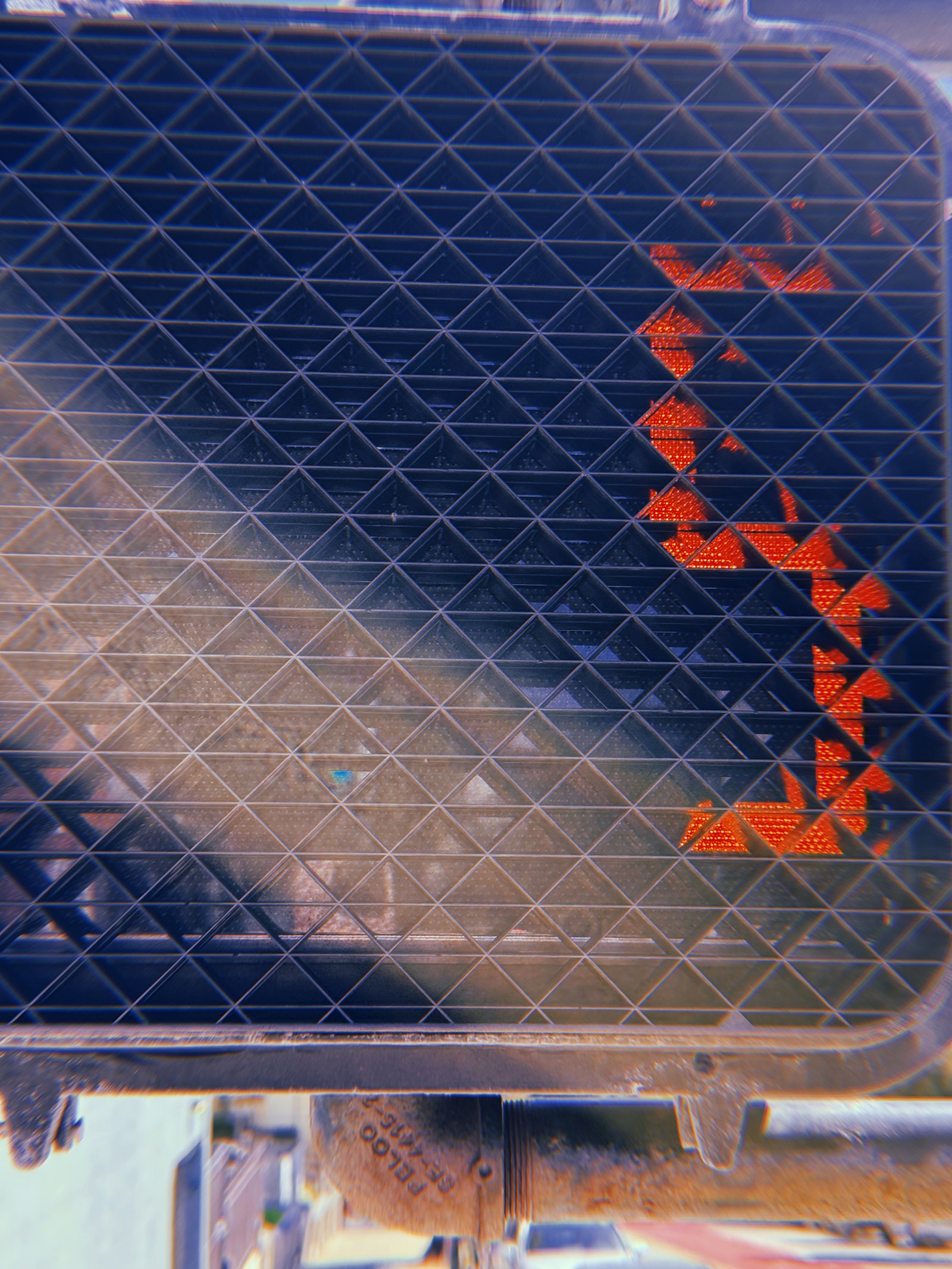 Red pedestrian countdown number 5 illuminated behind a black triangular protective grid, partially obscured by sunlight and reflections.