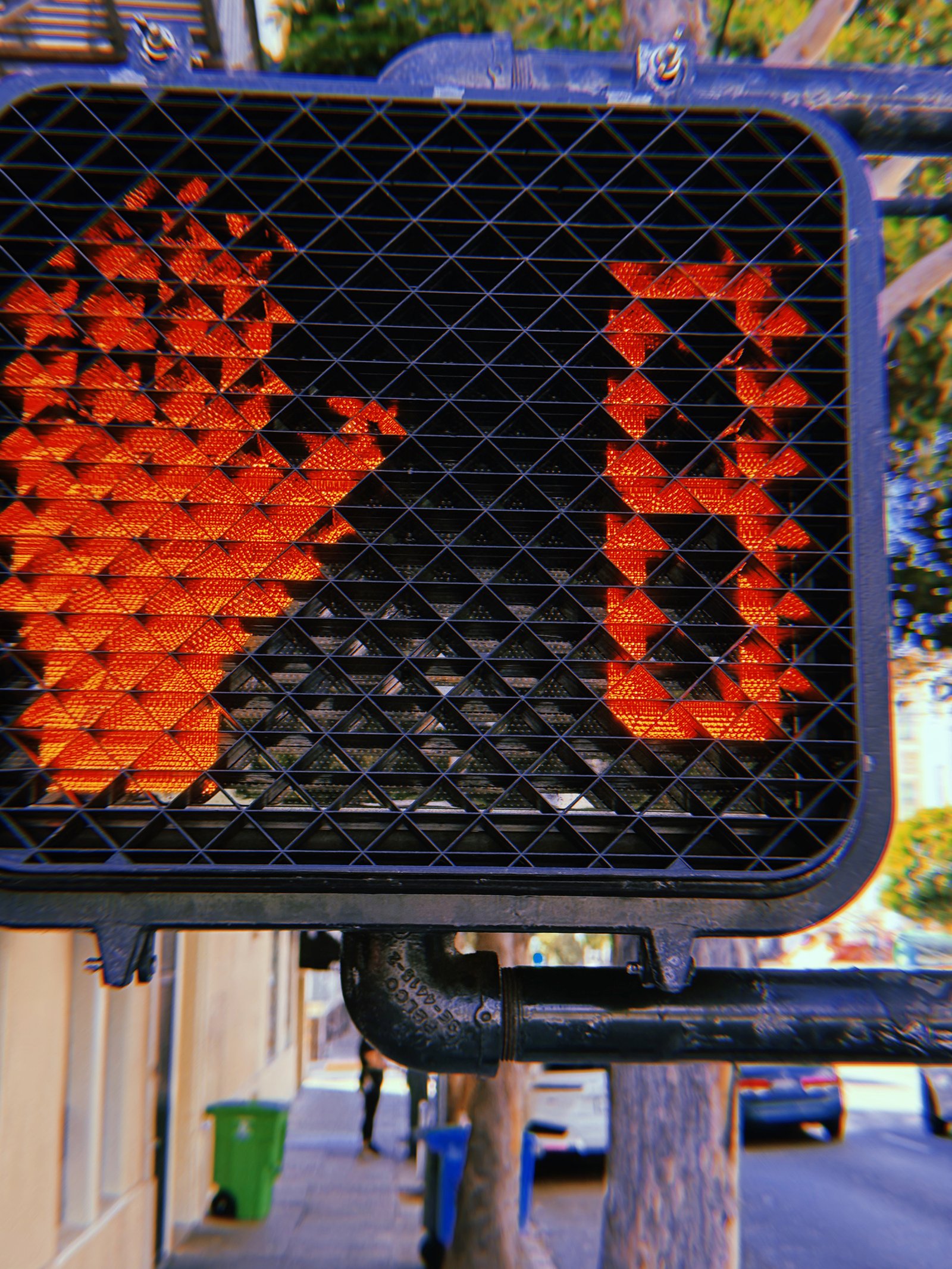 Red pedestrian stop-hand symbol and countdown number 9 illuminated behind a black geometric protective grid on a crossing signal in San Francisco.